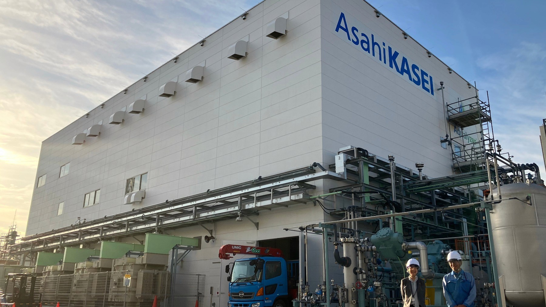 Asahi Kasei industrial facility with white building facade, external piping, scaffolding, and a delivery vehicle at ground level