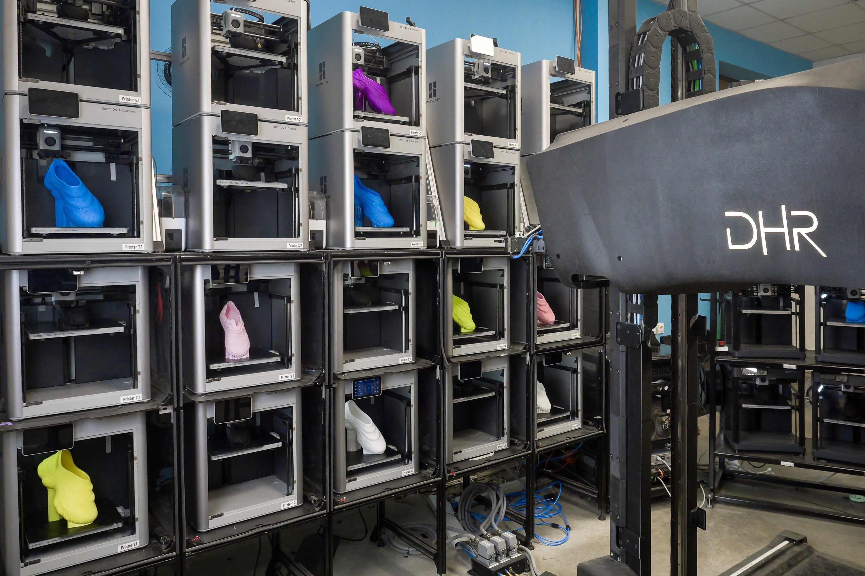 A wall of printers in a 3D print farm, producing 3d printed shoes.