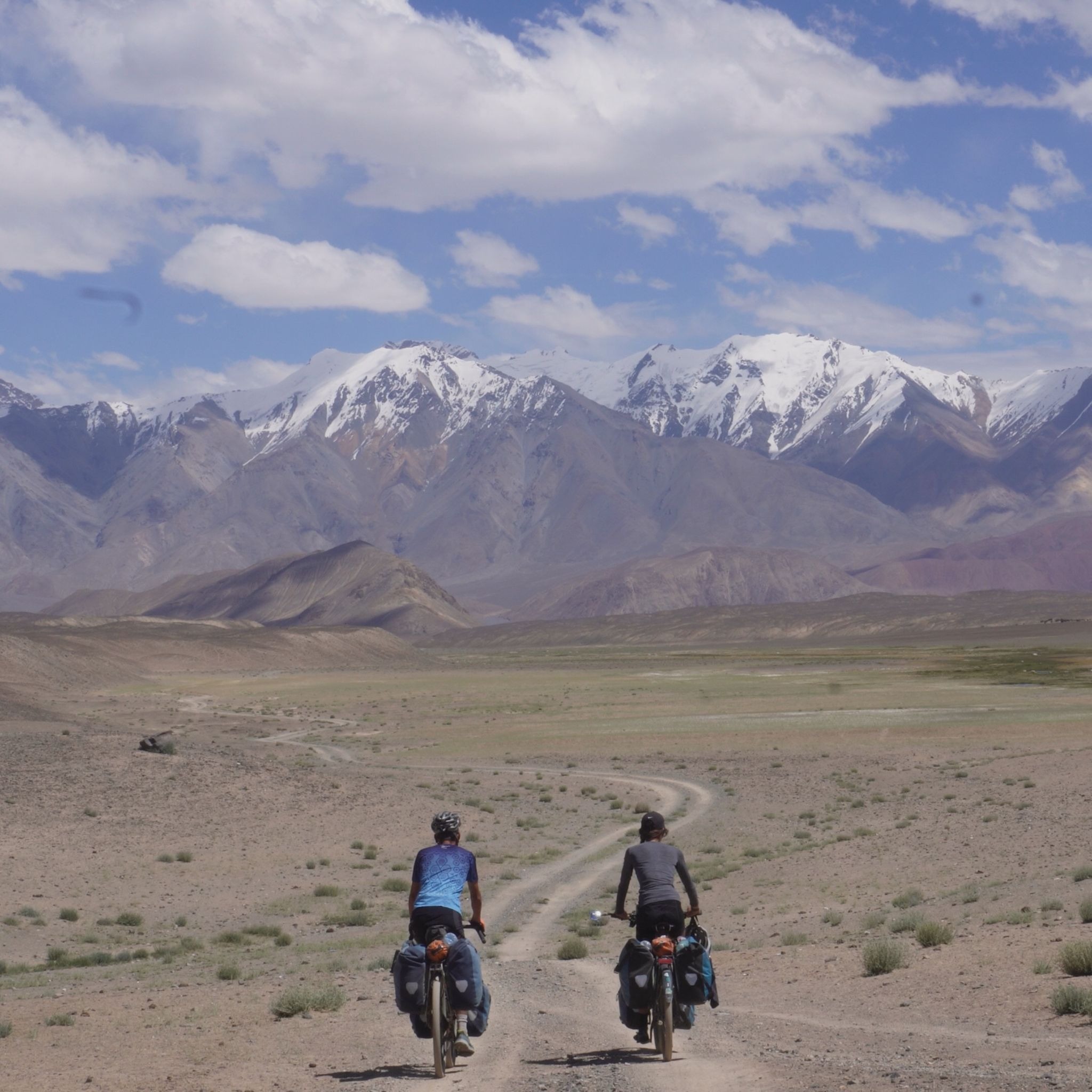 The backs of two long-distance cyclists, pedalling on an empty trail towards the Himalayas