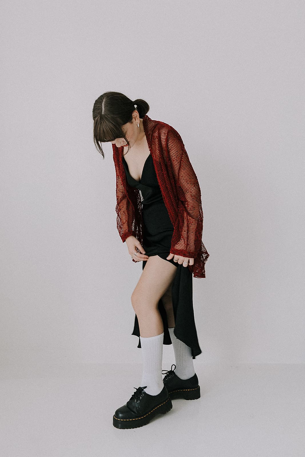 A model adjusting her black dress and red mesh jacket, showcasing the edgy 90s style at Revelator Studio, a natural light photography studio in Shreveport.