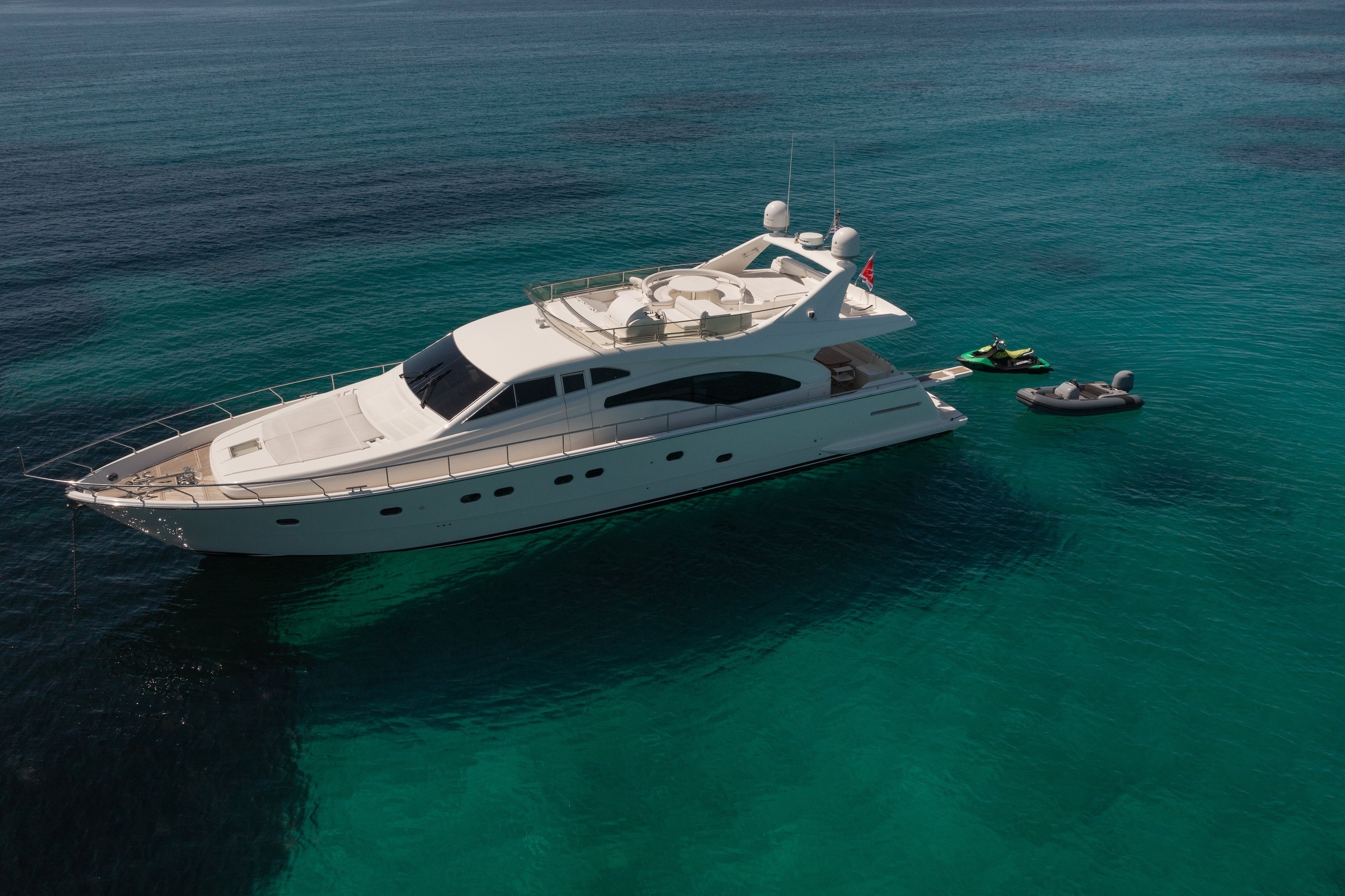 White Ferretti 68 motor yacht anchored in crystal-clear turquoise waters with inflatable tender and jet ski alongside.