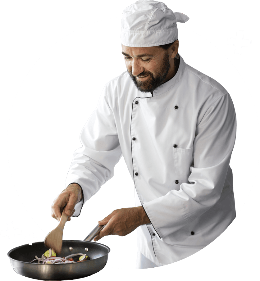 Na zdjęciu widać kucharza ubranego w klasyczny biały strój i czapkę kucharską. Trzyma patelnię, na której smaży kolorowe warzywa, m.in. czerwone cebule i cukinię, mieszając je drewnianą łopatką.
