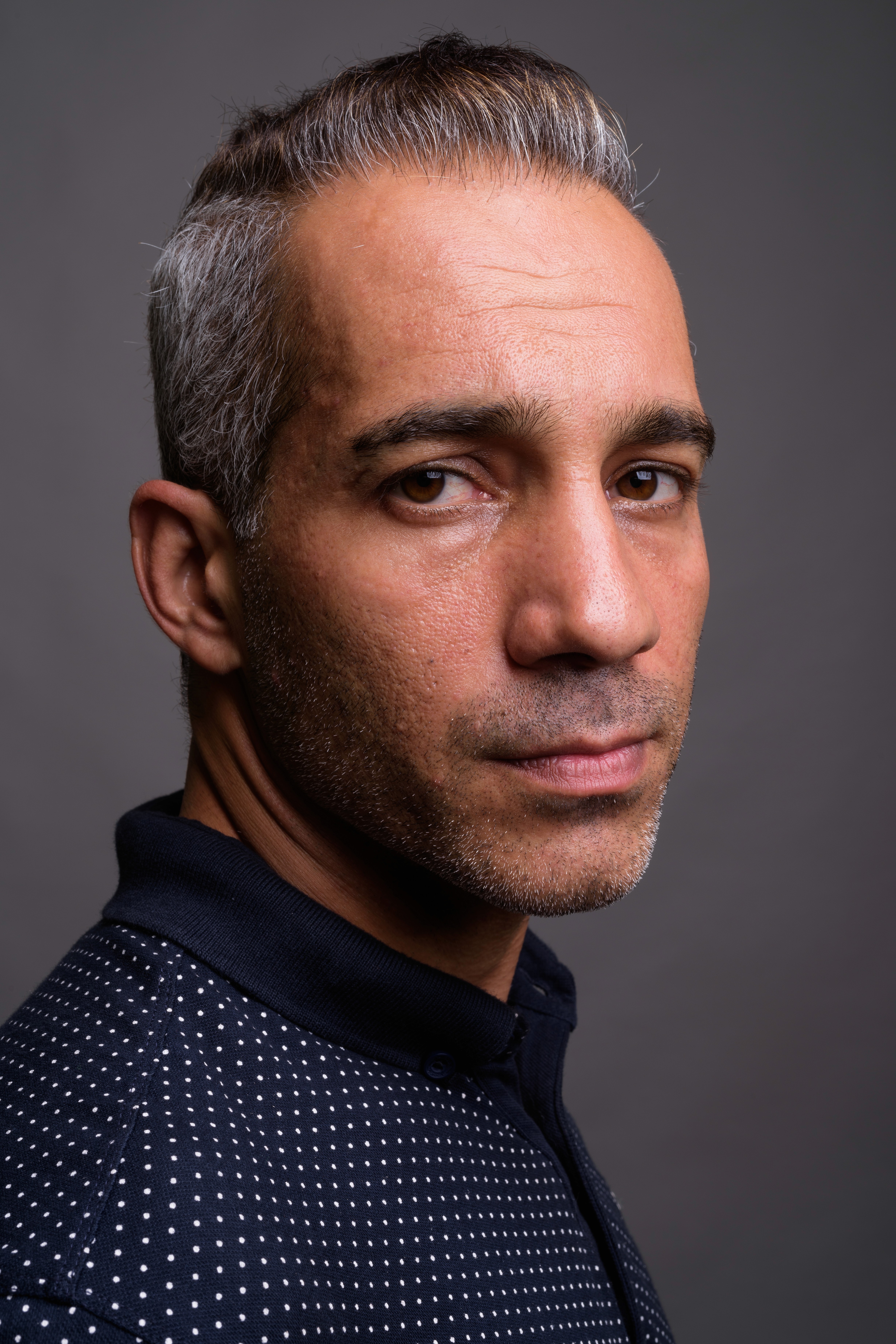 This portrait features a person with short hair and clear-framed glasses, capturing a direct and confident gaze into the camera.