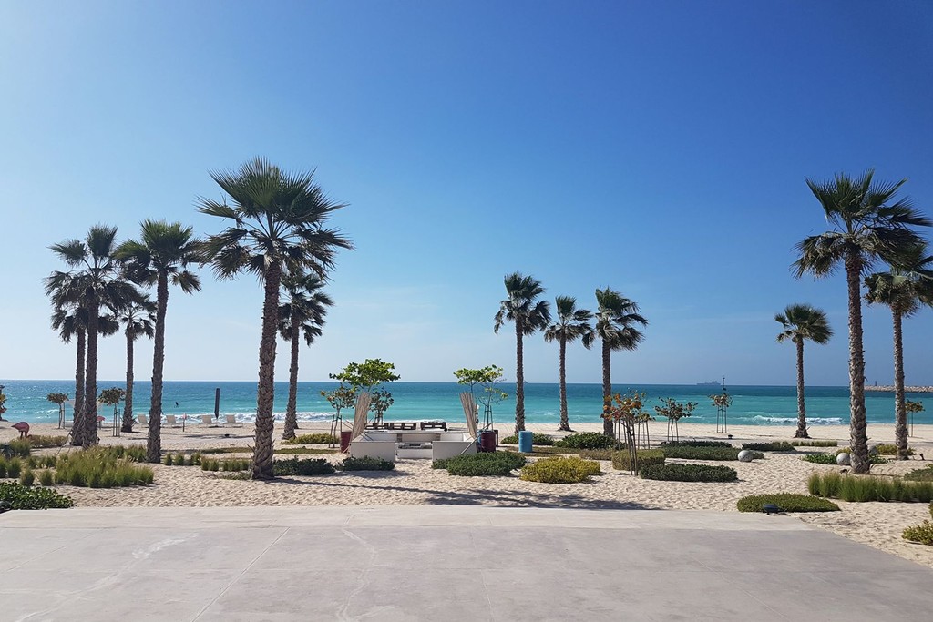 Tranquil Pearl Jumeirah beach with golden sand, turquoise waves, and lush palm trees, perfect for relaxation.
