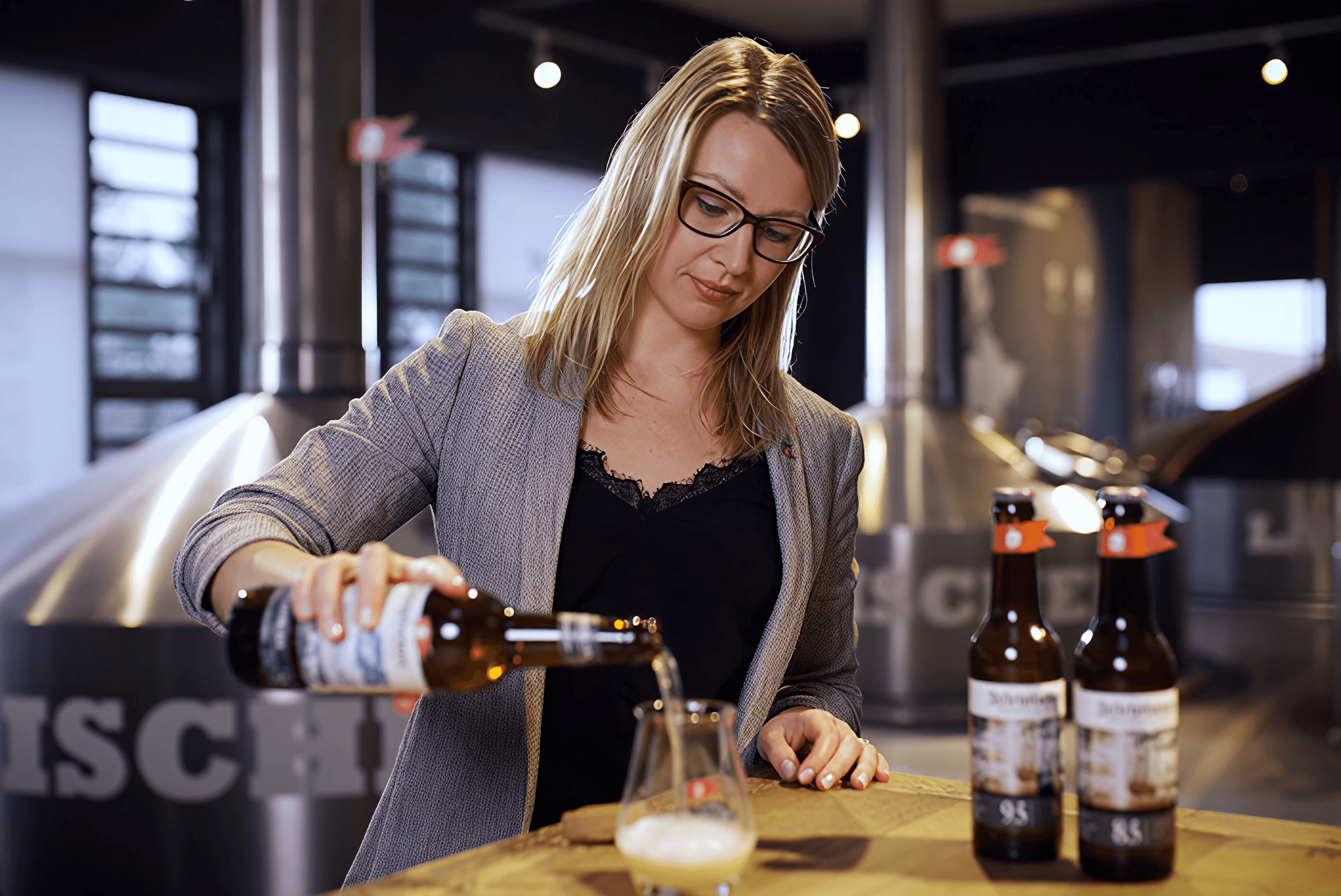 Woman pouring beer in brewery with tanks in background