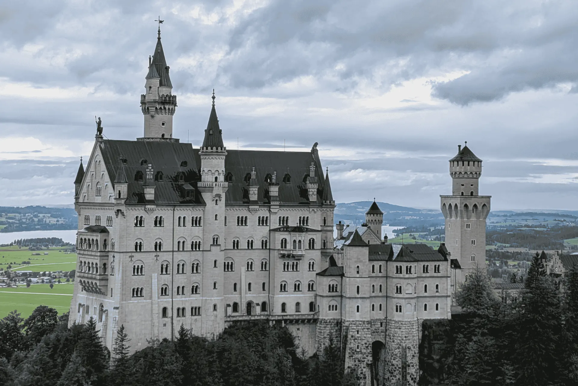 Schloss Neuschwanstein in Bayern, Deutschland, umgeben von grüner Landschaft und unter dramatischem Himmel.