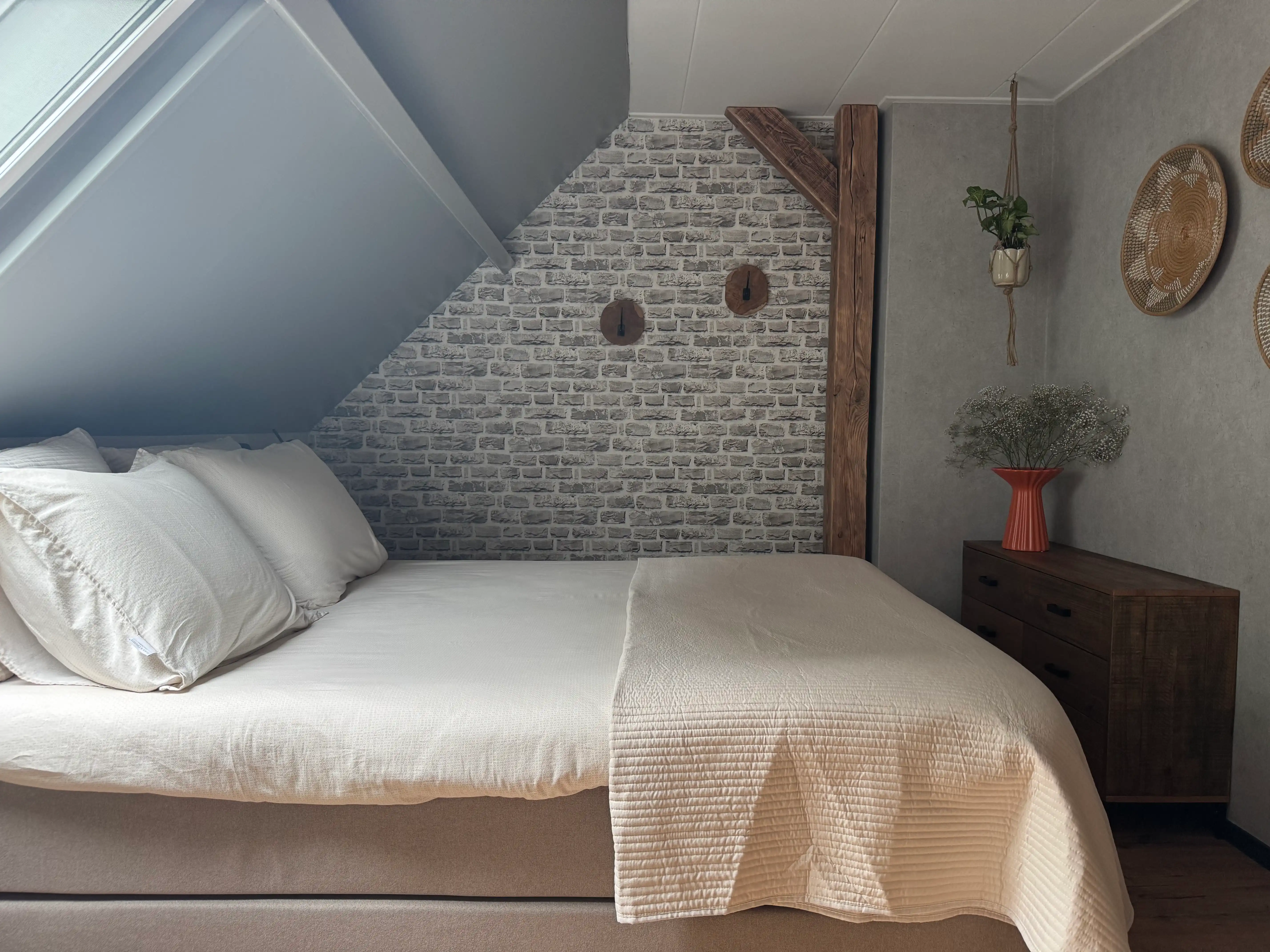 Boxspring tweepersoonsbed onder dakraam met zicht op stenen accentmuur.
