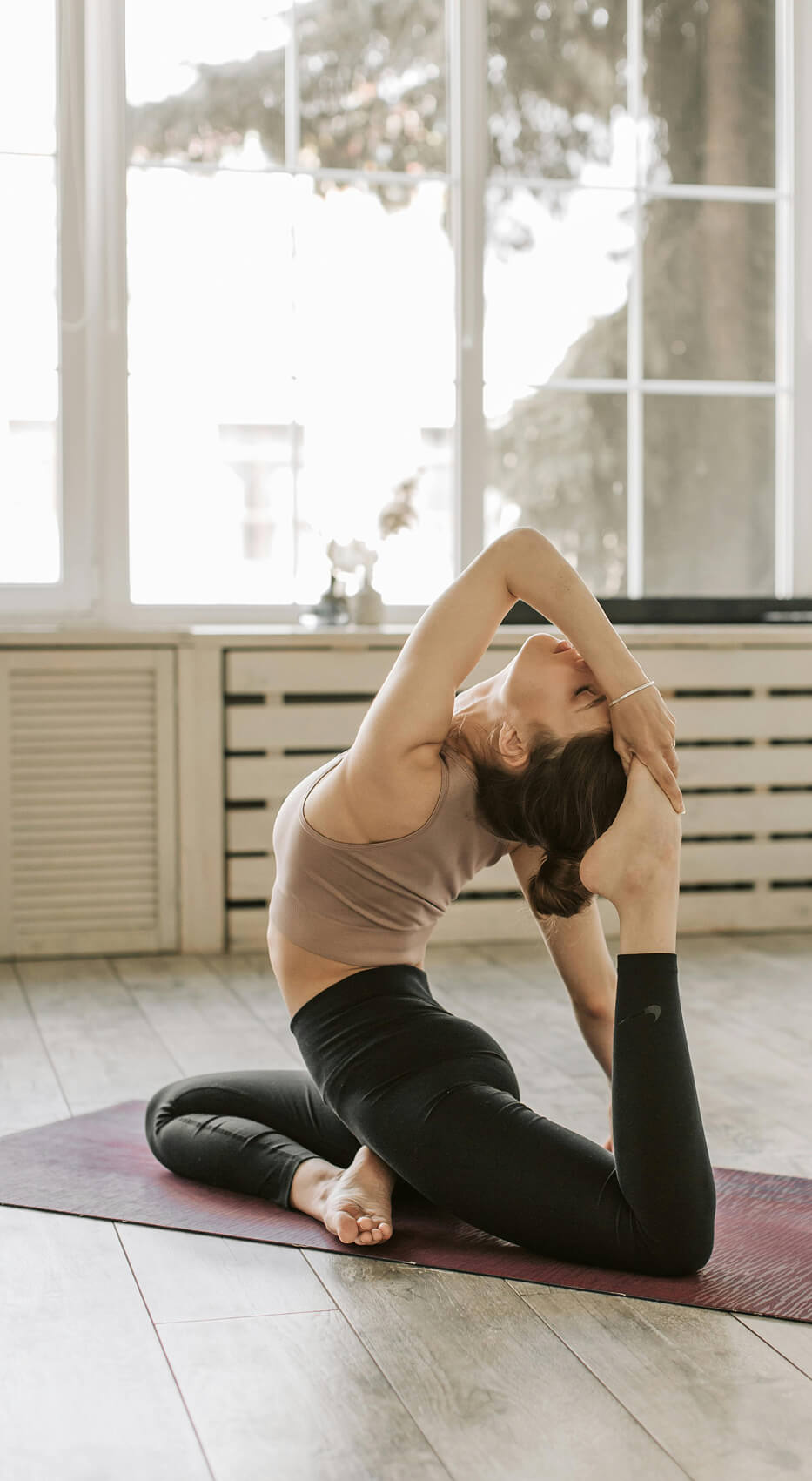Woman practicing an advanced yoga stretch on a mat in a bright studio