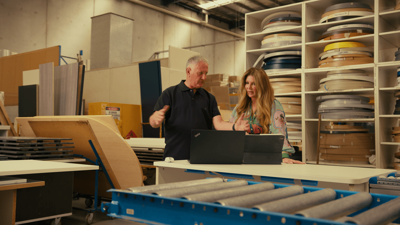 People working at desks in an office or workspace with shelves in the background
