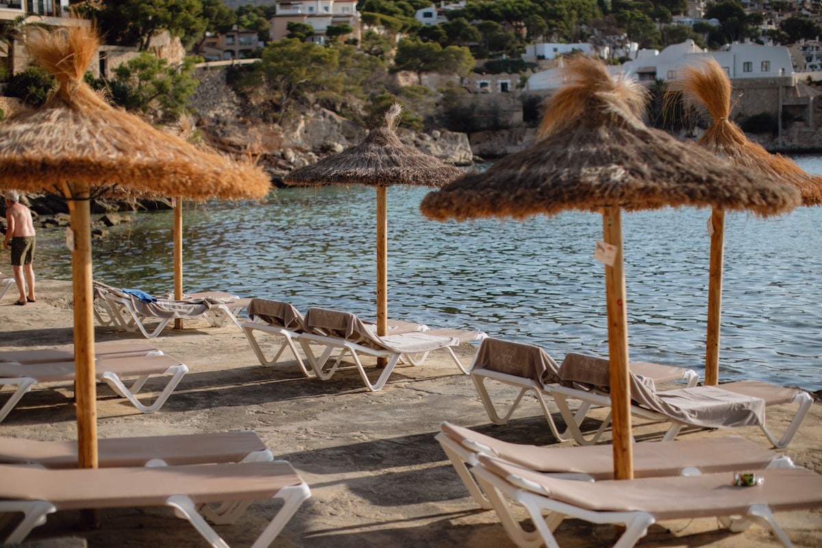 Row of beach loungers and umbrellas beside calm Mediterranean turquoise water on a Greek island