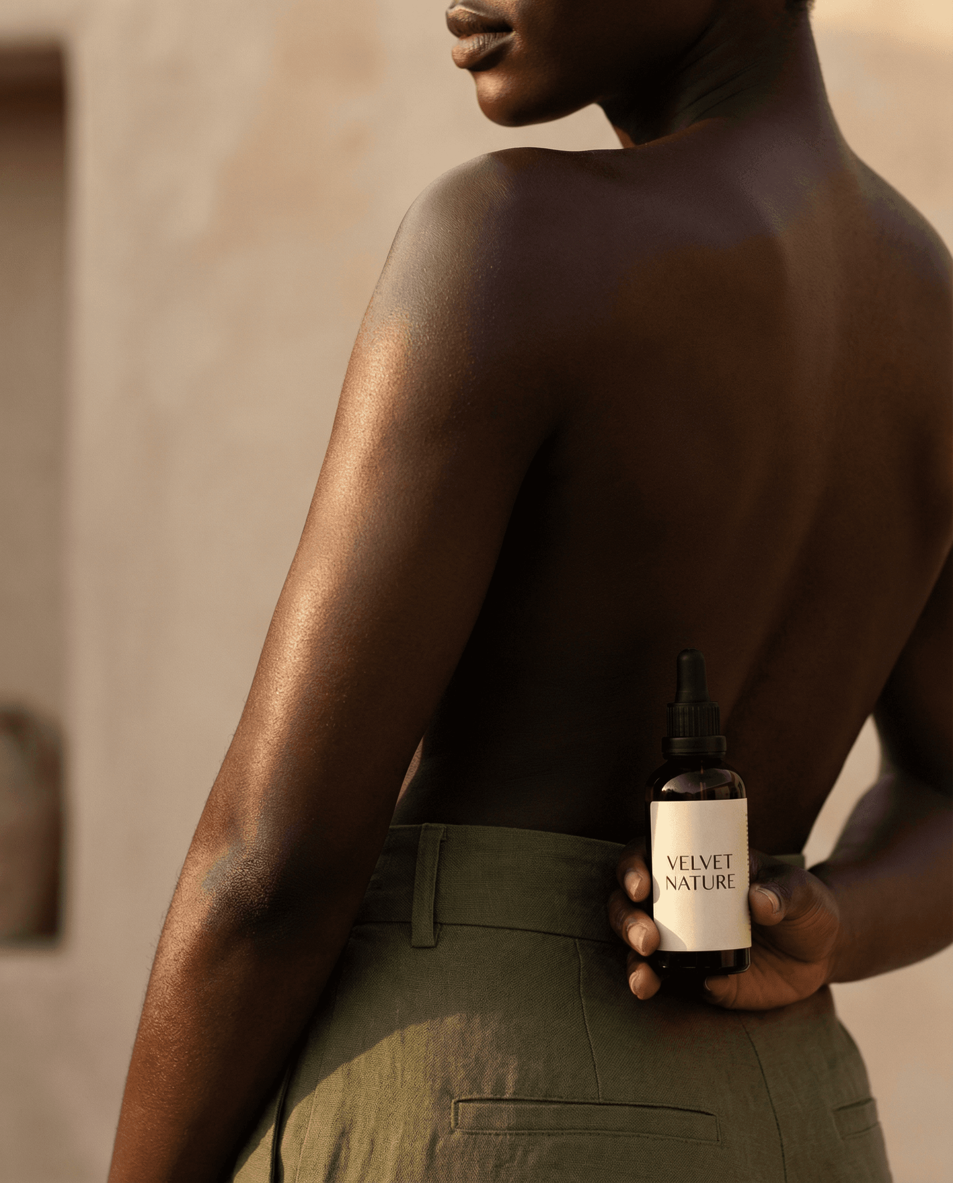 Velvet Nature facial oil serum bottle held behind model’s back with glowing skin