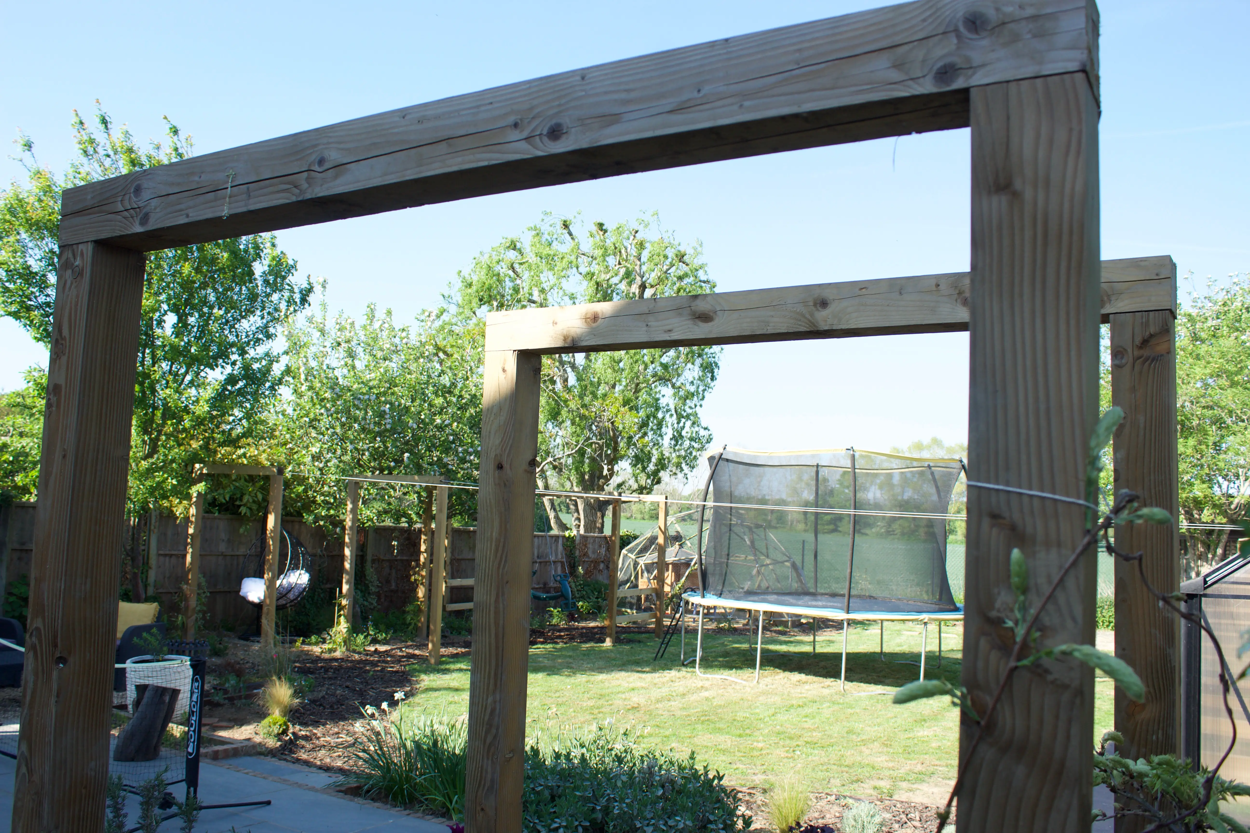 A wooden structure frames a green park area with trees and a grassy space in the background.