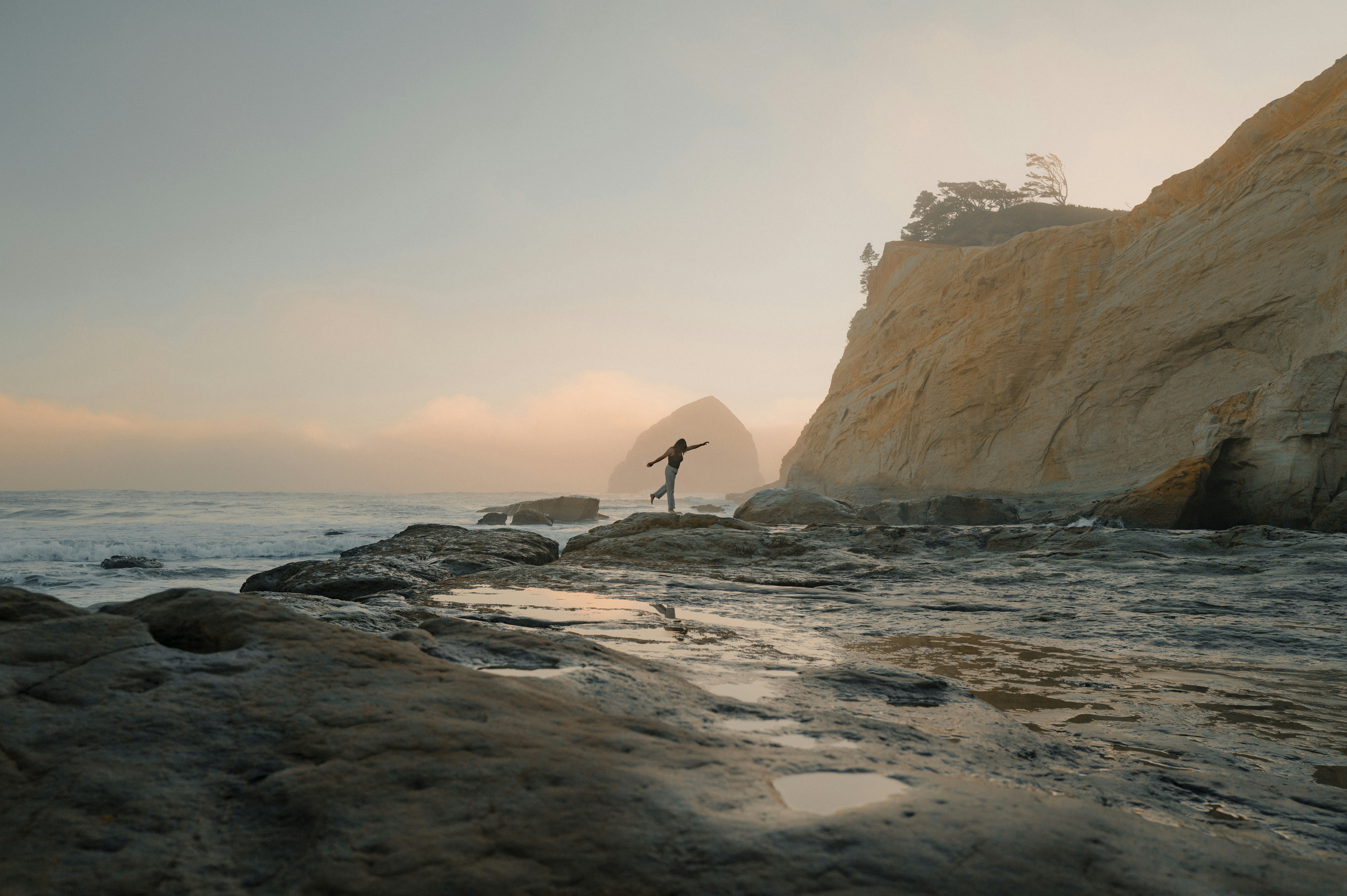 Person balancing on rocks by the ocean at sunset