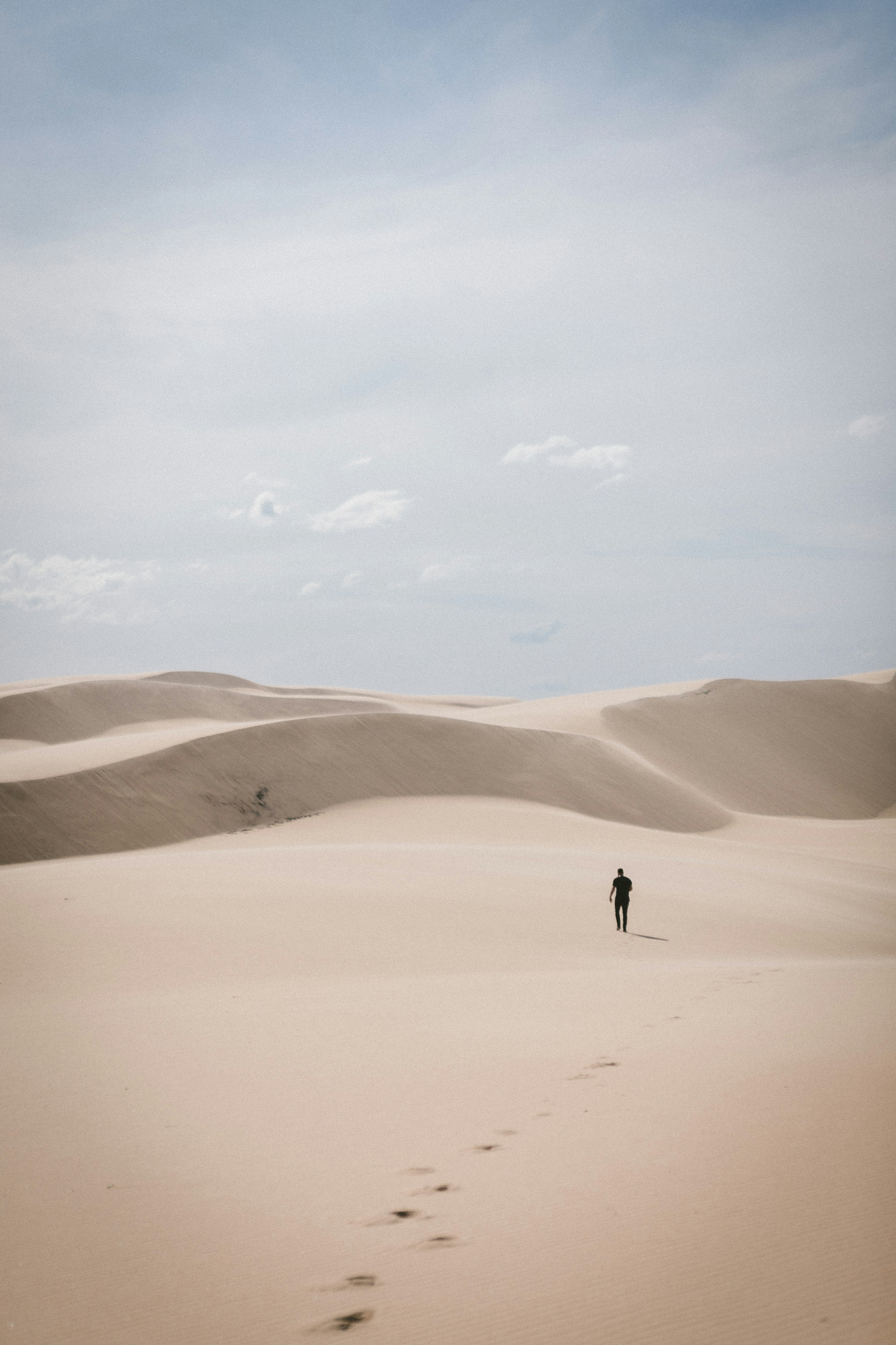 A long range image of man walking alone in the desert towards a dune on a hot day