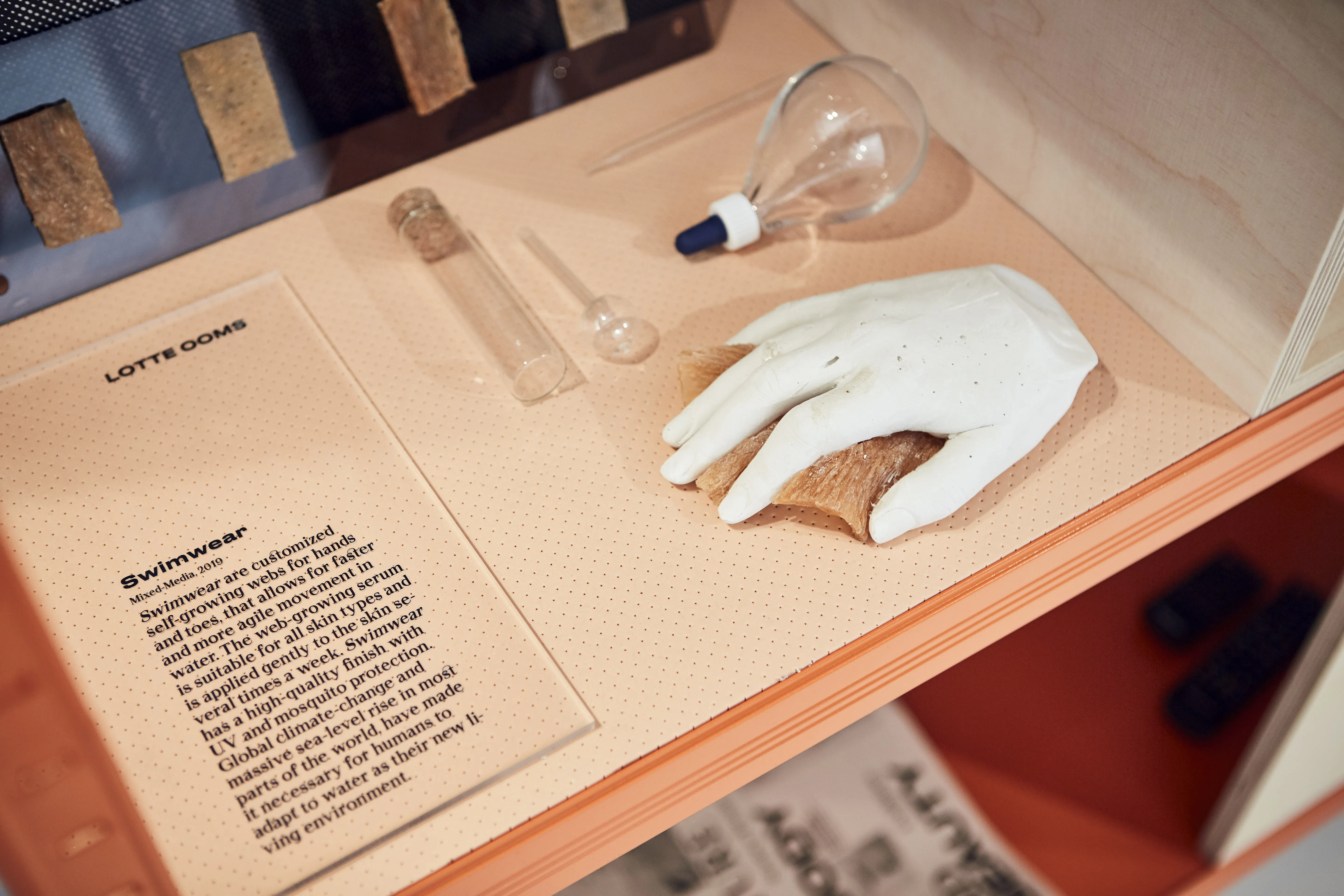 Display detail with a white sculpted hand, glass instruments and a text panel on customized swimwear at the Cosnova exhibition.