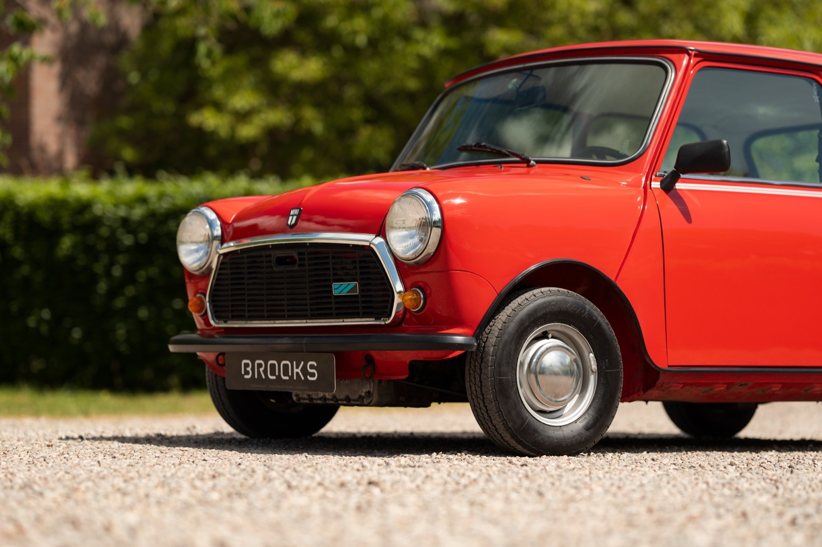 A classic red car parked on a gravel surface with greenery in the background.