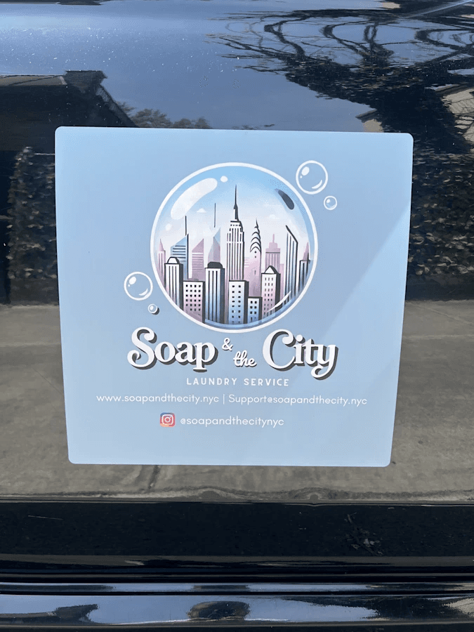 Soap and the City branded car magnet showing NYC skyline logo, website URLs, and Instagram handle, displayed on the side of a black vehicle to advertise pickup and delivery laundry service.
