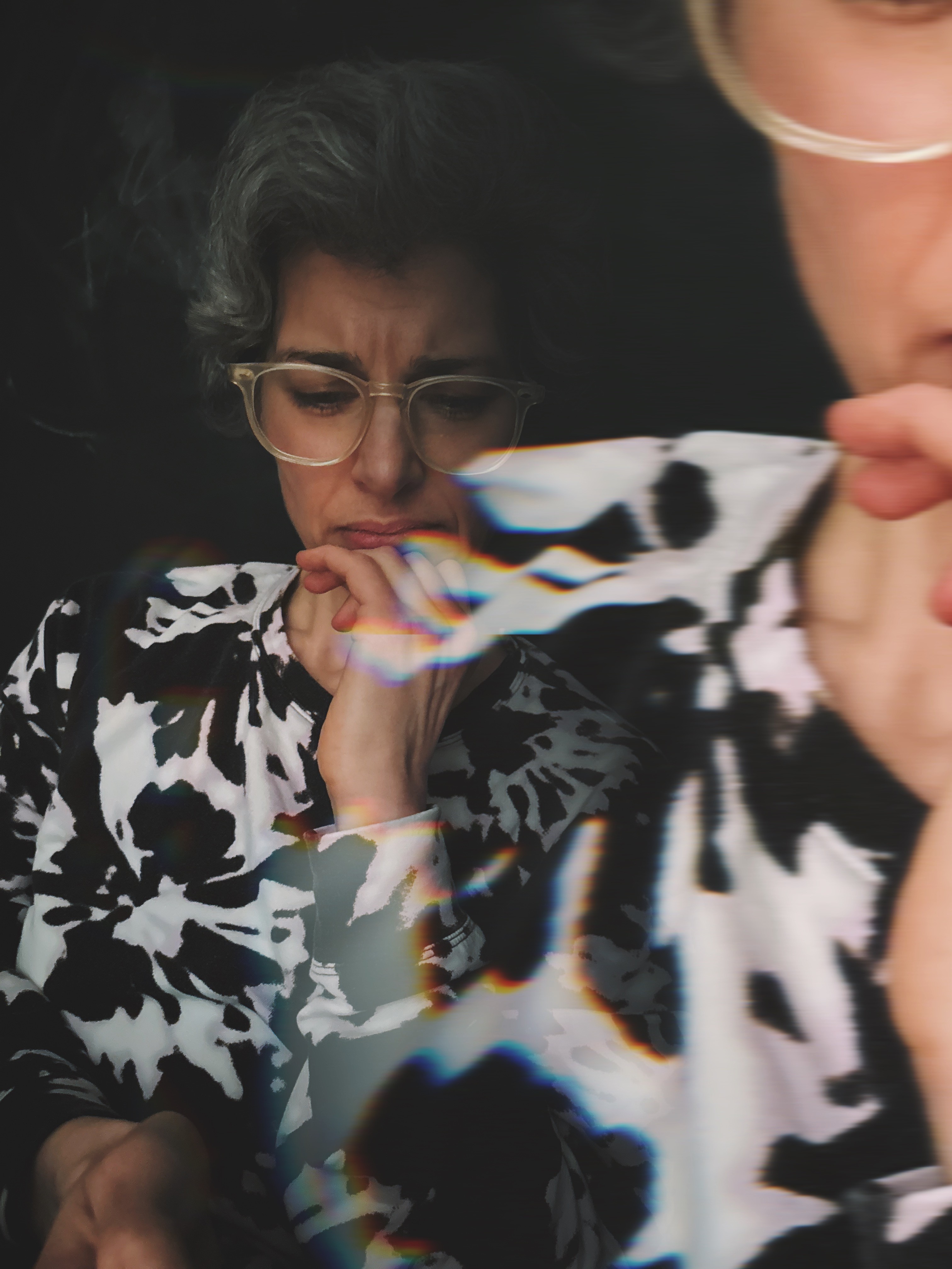 An older lady wearing glasses and a tie dye sweatshirt in black and white looking thoughtful with her hand on her mouth and her brow furrowed, looking downward at something. Image by Craig Hooper.