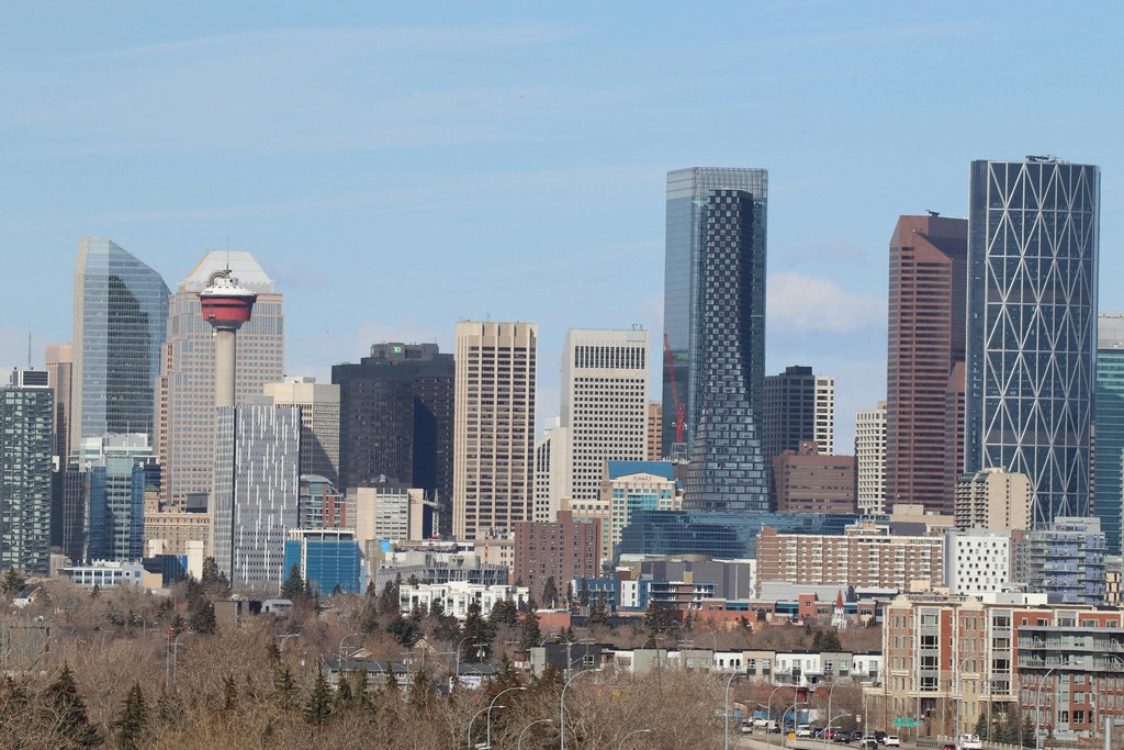 A modern daytime view of the downtown Calgary, Alberta skyline featuring the iconic Calgary Tower and modern glass skyscrapers reflecting in the water, representing a vibrant, affordable alternative with higher average salaries for newcomers comparing Calgary to Vancouver in 2026.