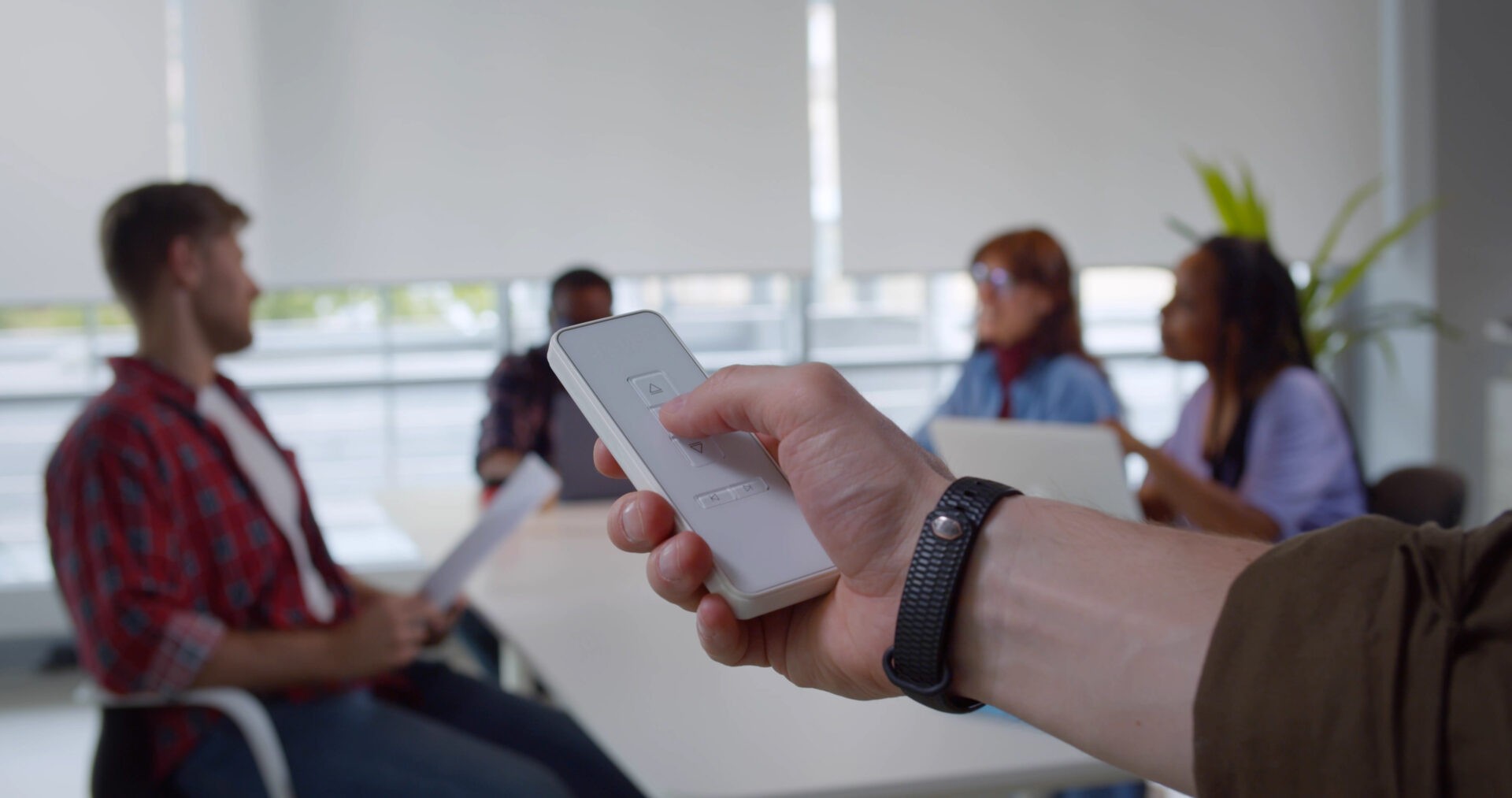 Close up of man's hand holding a remote control to close automated custom window blinds in an office. Wholesale Blind Factory