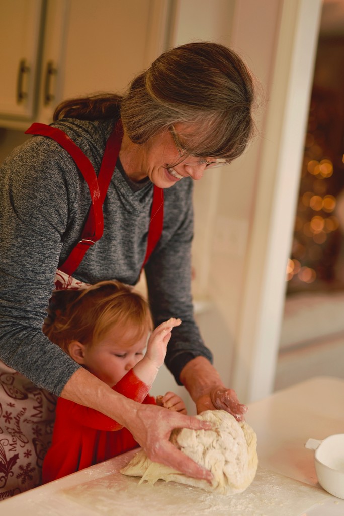 A smiling grandmother and her young granddaughter knead dough together in a cozy kitchen, highlighting a heartwarming moment of family bonding and holiday baking.