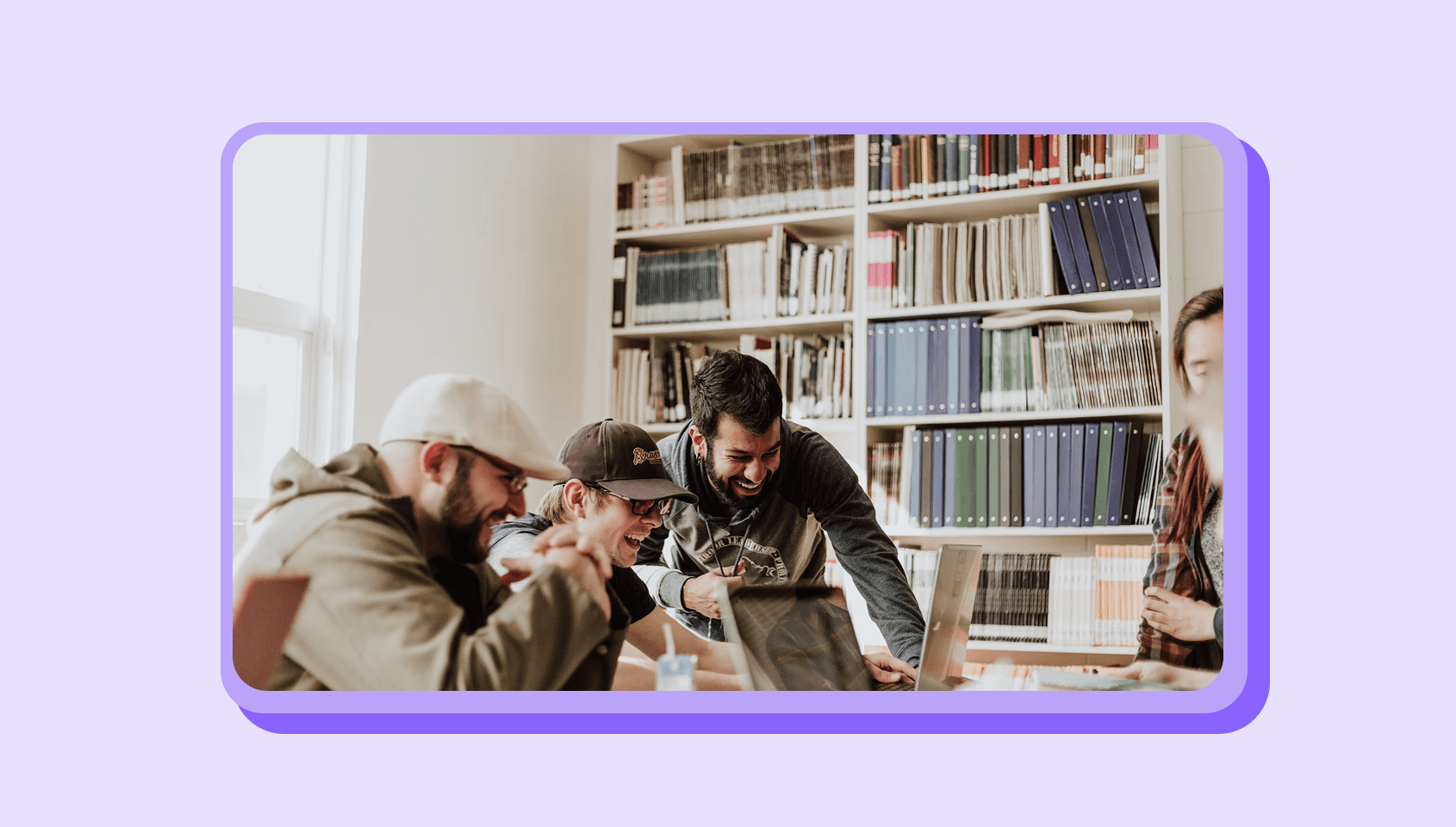Three people are laughing by seeing at a laptop in a library.