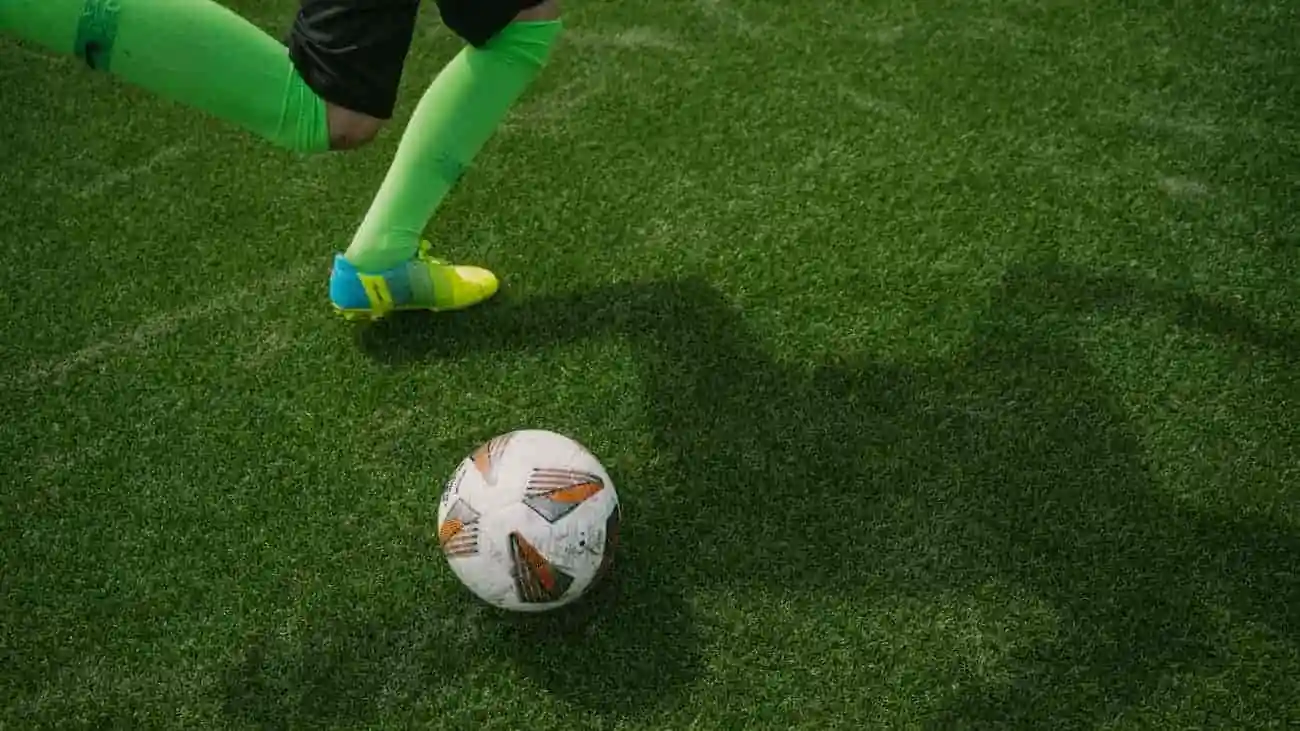 Football player in motion kicks a white ball on green grass, illustrating the dynamics and precision in football, relevant for the free tournament design on the CoachingArea platform.