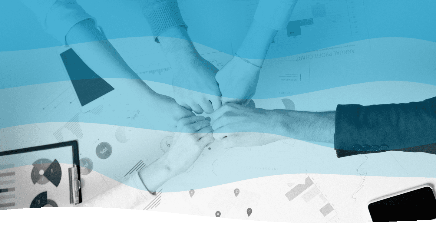 Five people gather their hands in a fist bump over a table with business documents, a tablet, and a smartphone, symbolizing teamwork and collaboration.