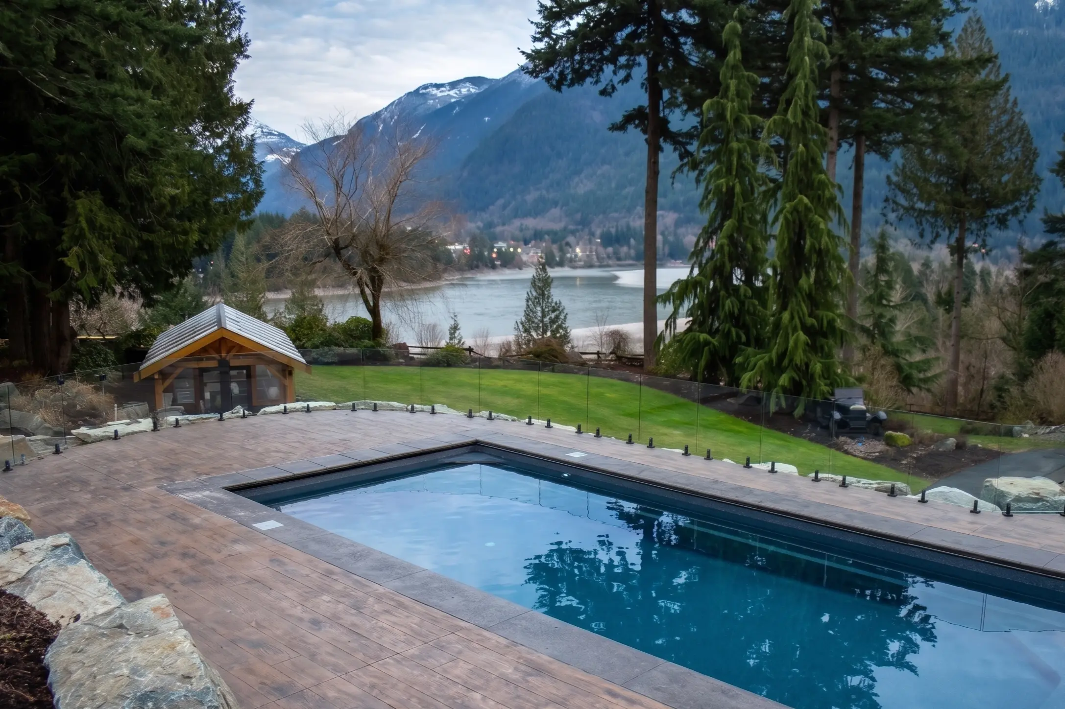Spigot glass railing on a pool deck with stainless steel spigots holding clear 12 mm glass panels above a Fraser Valley view.