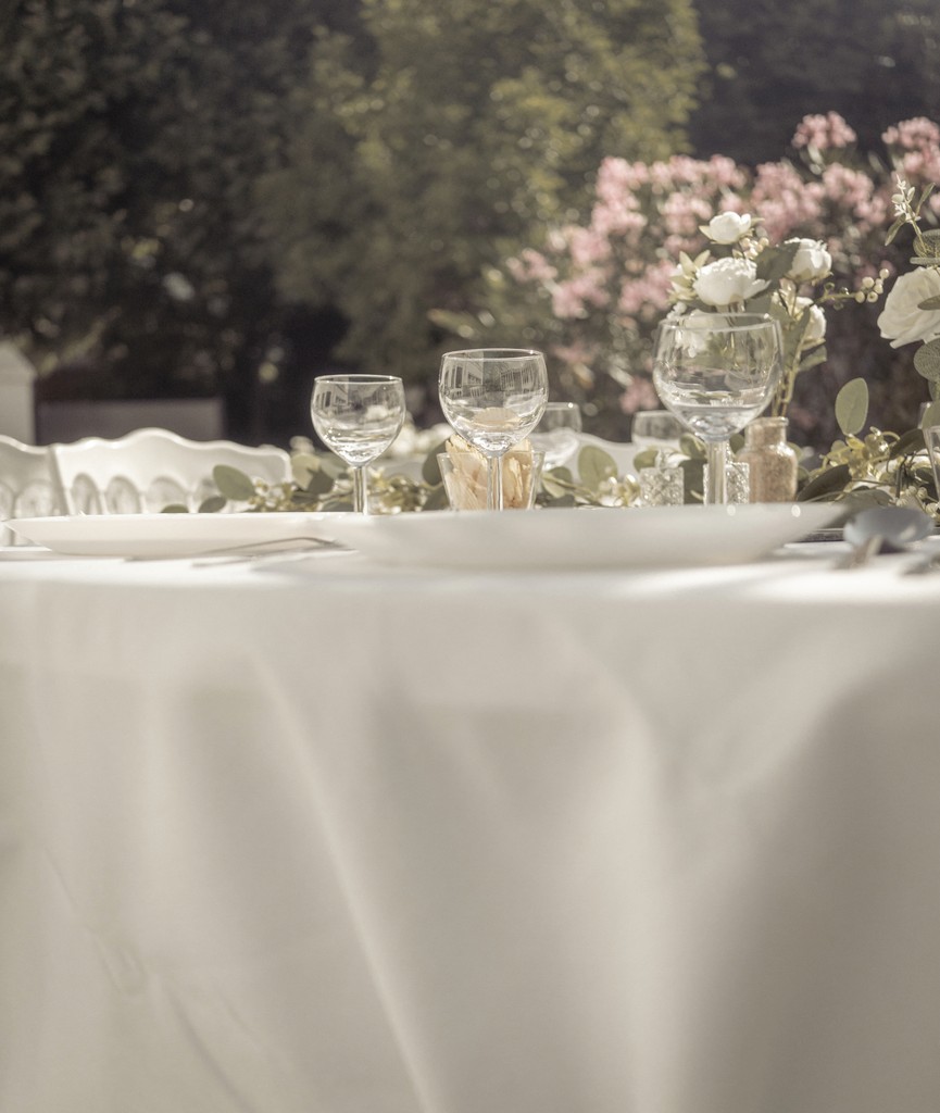 Elegant outdoor wedding table with crystal glasses and floral arrangements bathed in soft sunlight — fine art event photography. Table de mariage élégante en extérieur avec verres en cristal et compositions florales baignées de lumière douce — photographie Fine Art d’événement.