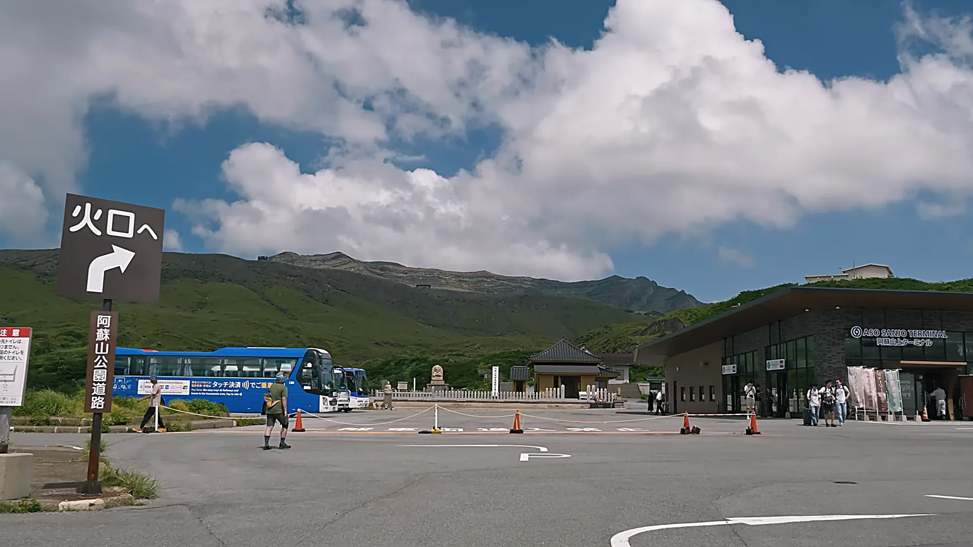 A sign reading to the crater at the Aso volcano visitor centre, buses waiting beyond