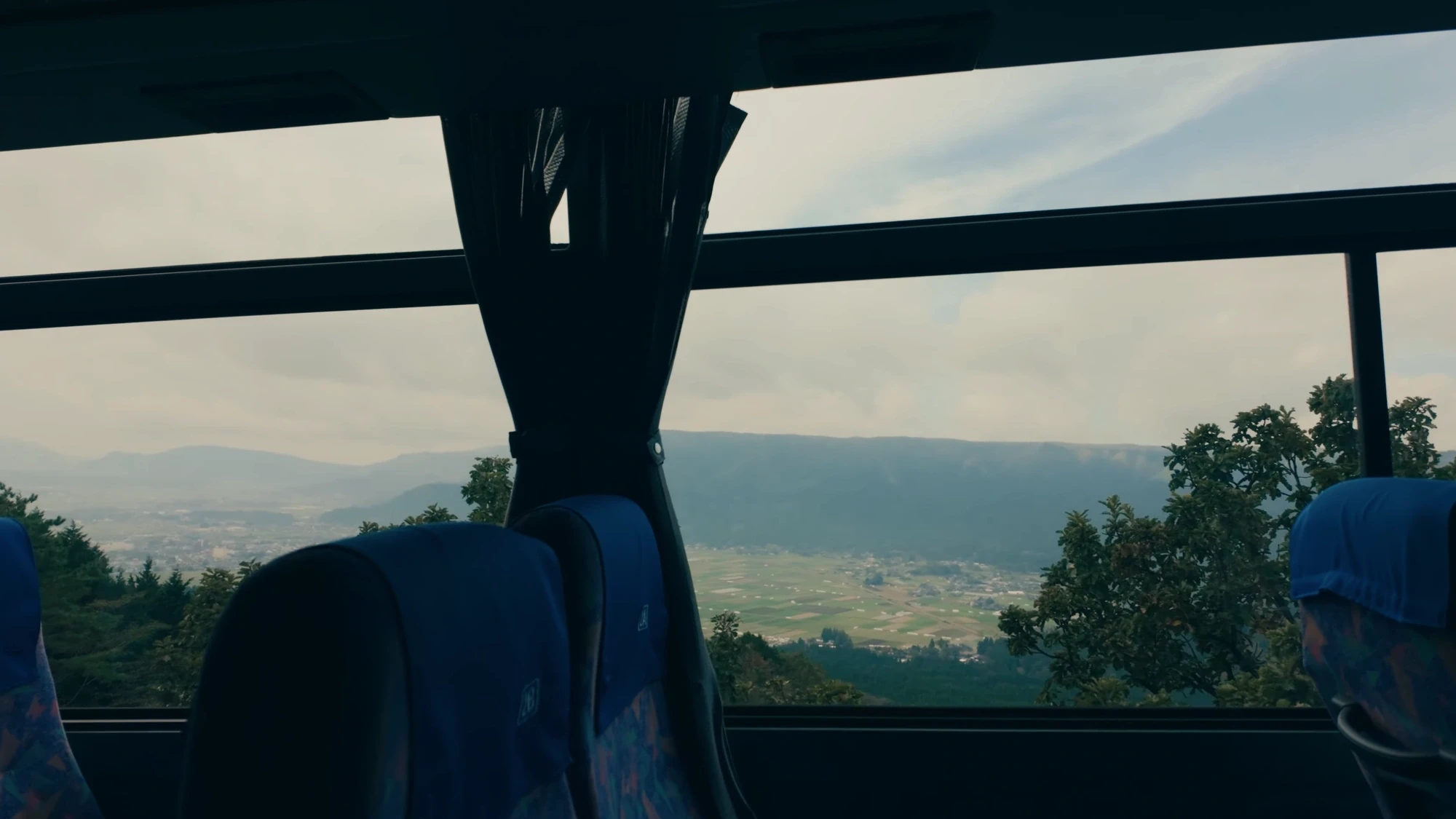 The view forward from a highway bus crossing the Aso caldera, farmland on the crater floor below the outer rim