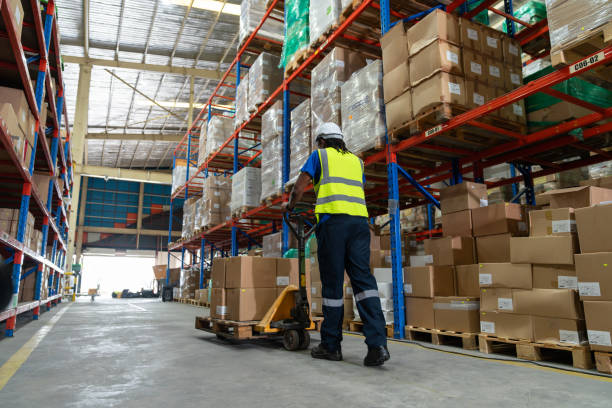Person operating a pallet jack to move a pallet through the warehouse