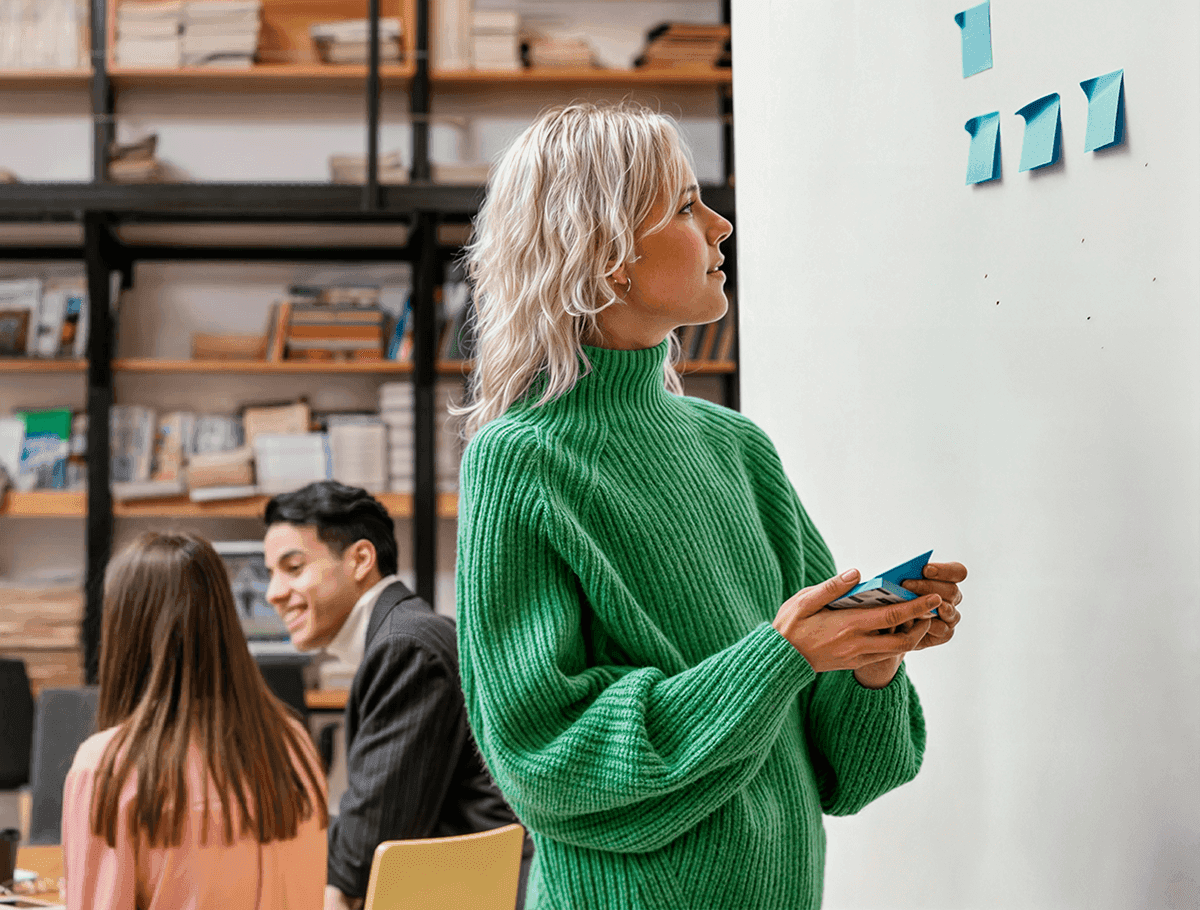 A woman in a green sweater looking at post-it notes on a wall.