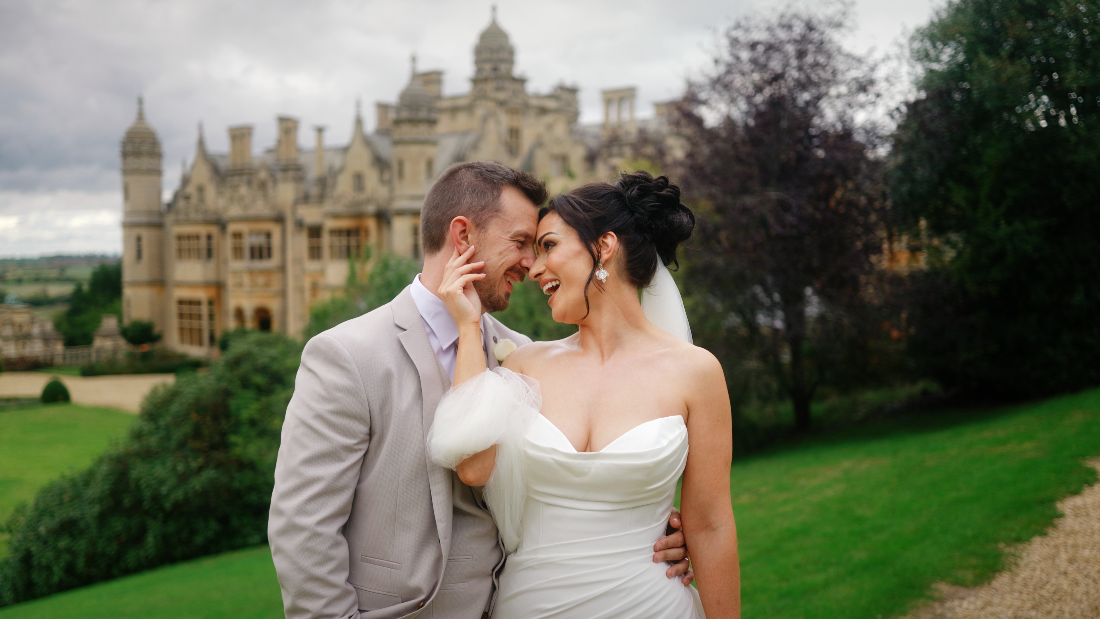 Bride and groom sharing a joyful moment during wedding portraits at Harlaxton Manor in Lincolnshire, with the historic house and gardens behind them