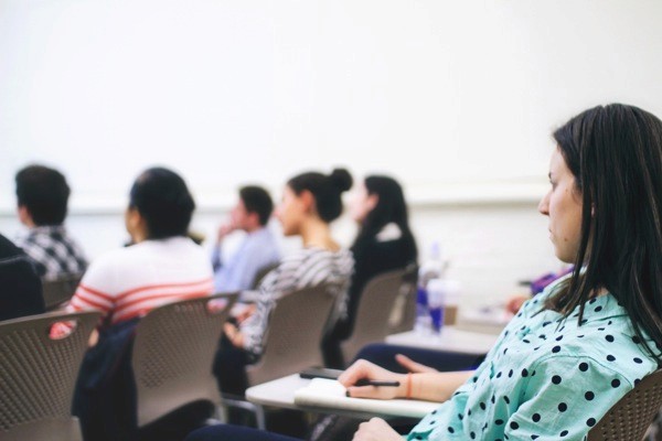 A photo of a group of people siting in a classroom, taking notes and listening to a lecture.