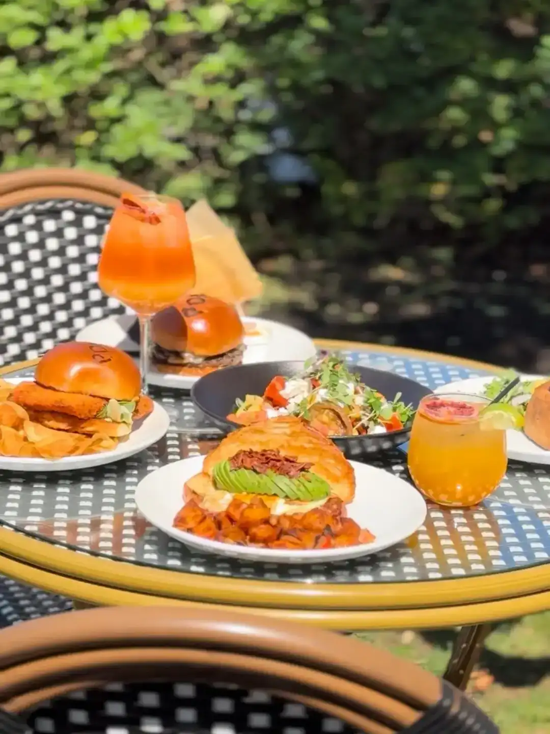 Outdoor table featuring gourmet burgers and fresh cocktails at Pain D’Avignon Chatham patio.