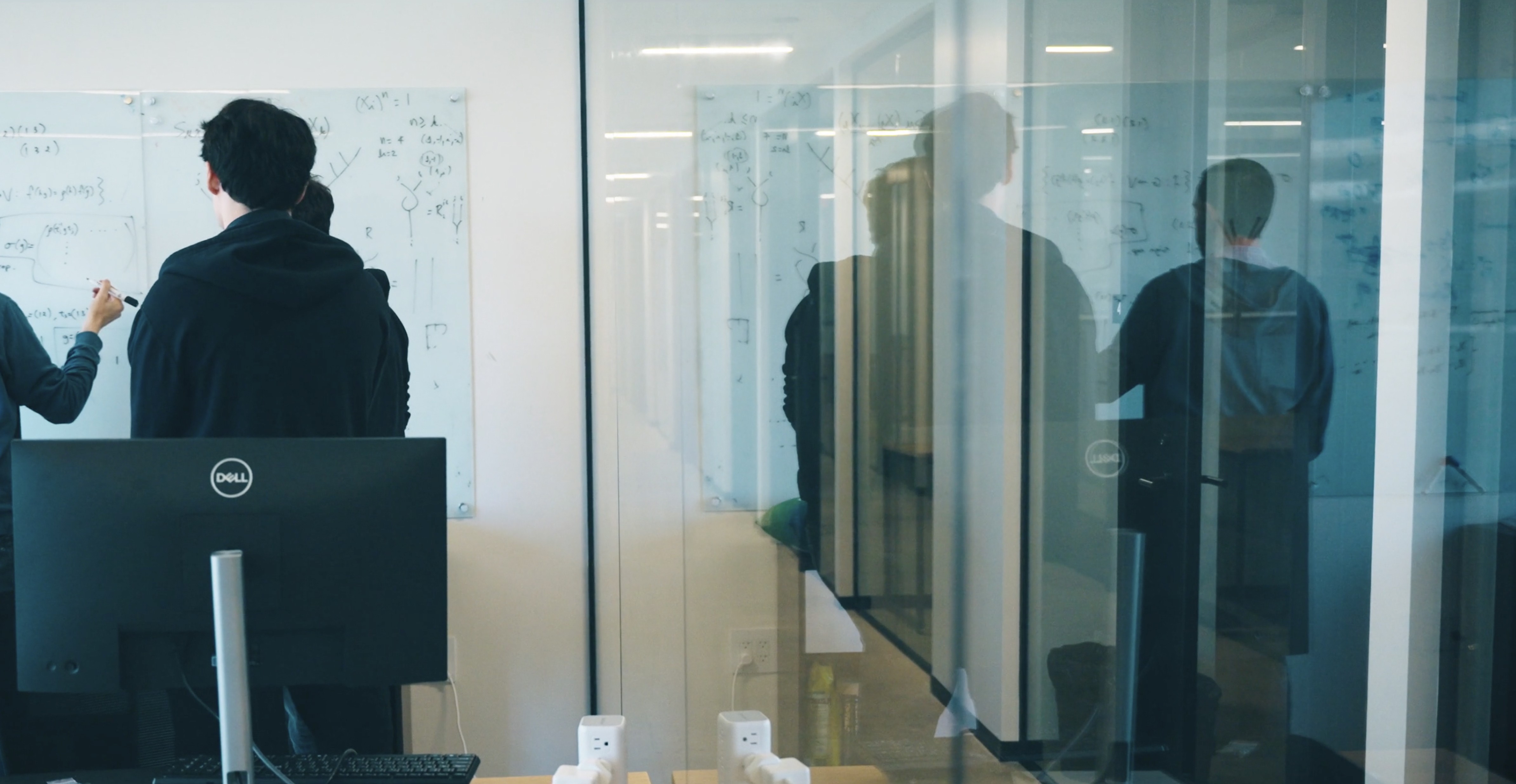 Woman looking at a computer screen in warm natural light, focused and thoughtful, with sunlight casting soft shadows on the wall behind her.