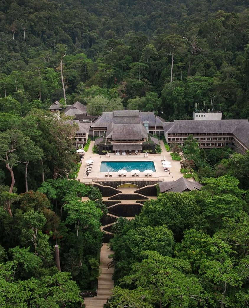 Aerial view of The Datai Langkawi resort surrounded by lush rainforest, featuring a pool and landscaped pathways.