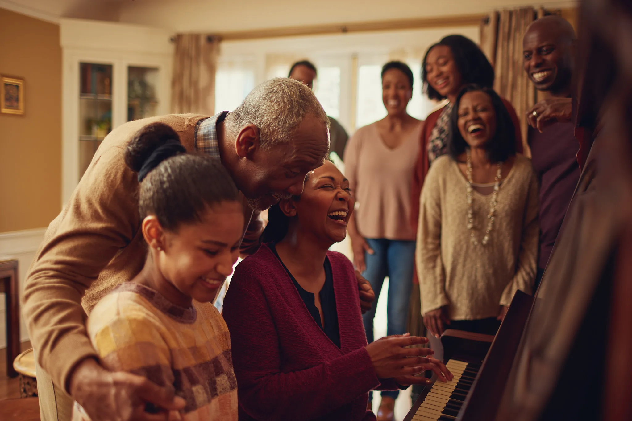 family gathers around woman playing piano — lifestyle photography by Tom Kubik