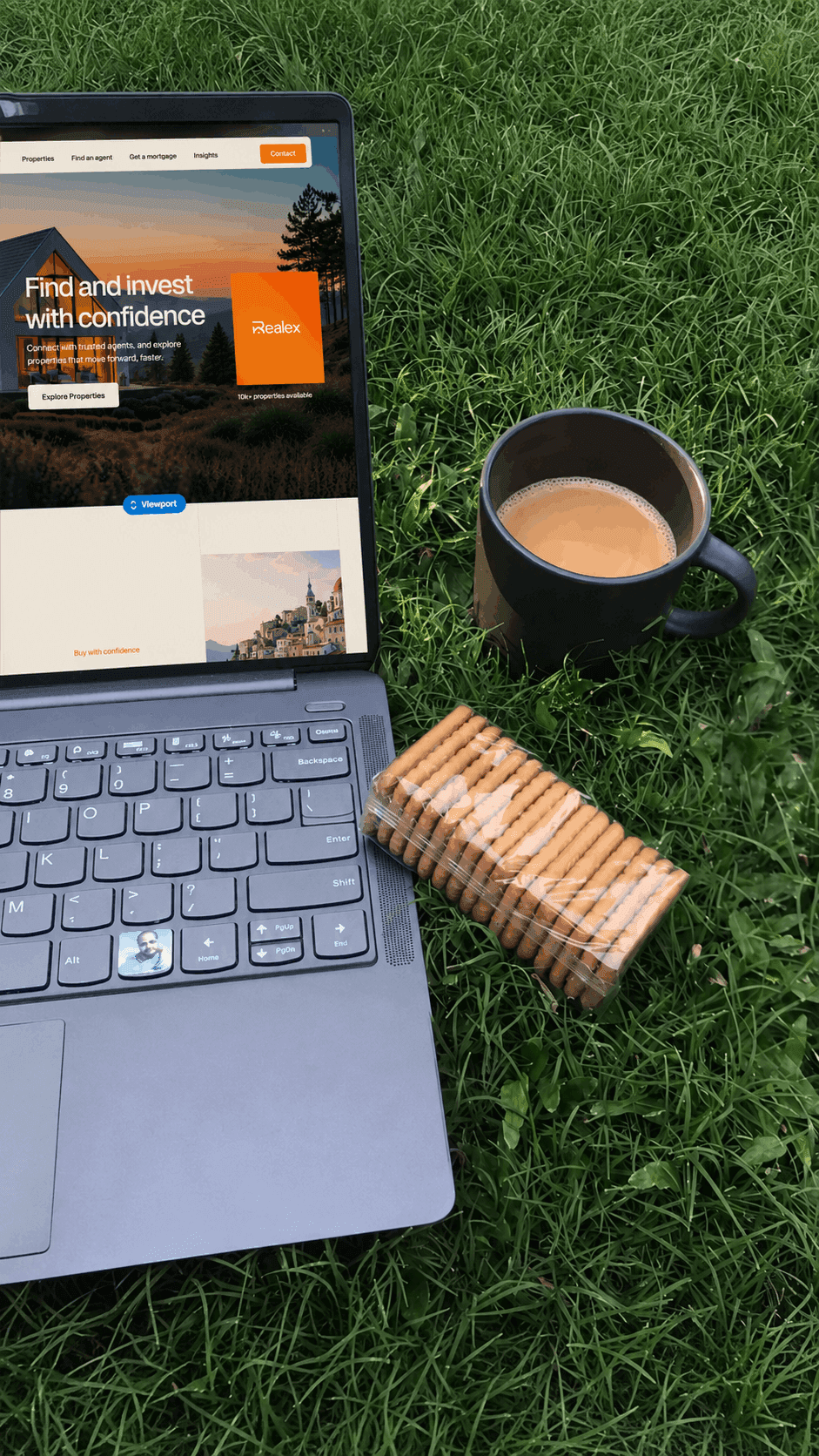 A laptop and a cup of coffee placed on green grass, suggesting a relaxed outdoor workspace.