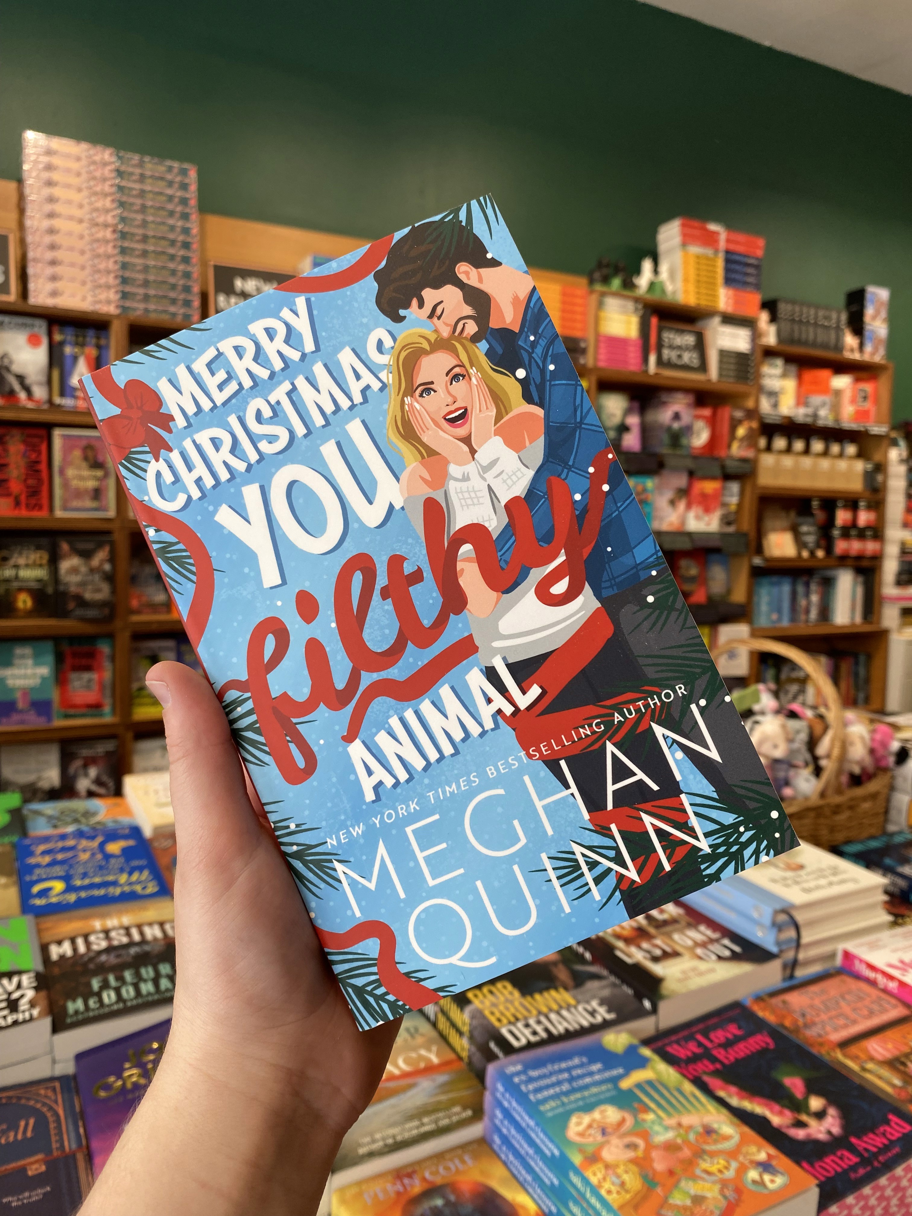 A hand holding a copy of Merry Christmas You Filthy Animal by Meghan Quinn