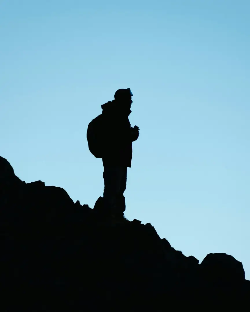 silhouette of a hiker standing on a mountain at dusk