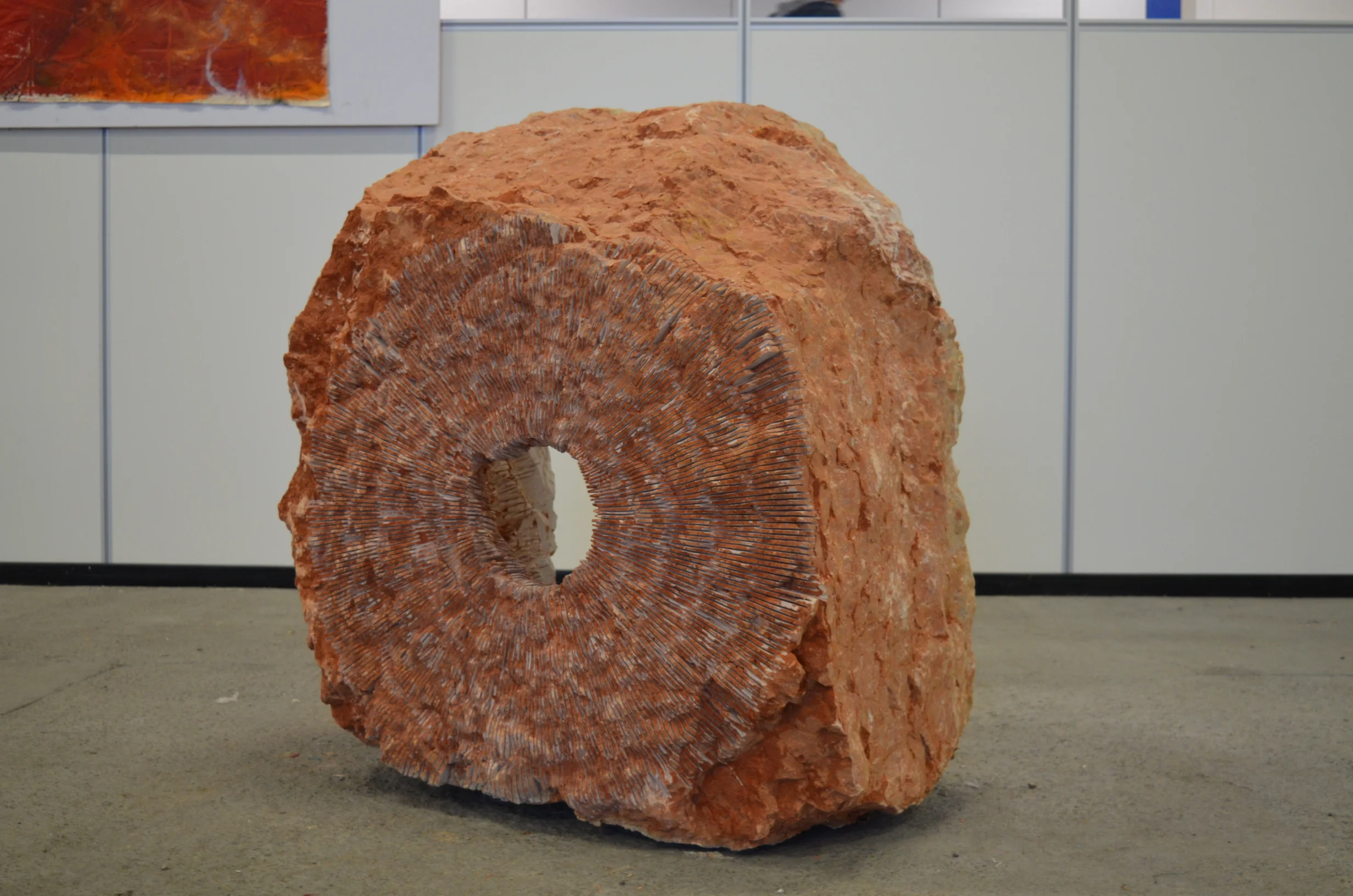 Installazione iStone Arte con blocco di pietra rossa lavorata e opera murale radiale contemporanea, sinergia tra arte materica e design per brand