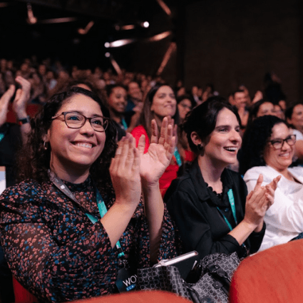 Smiling woman sitting at desk with a computer, surrounded by plants.