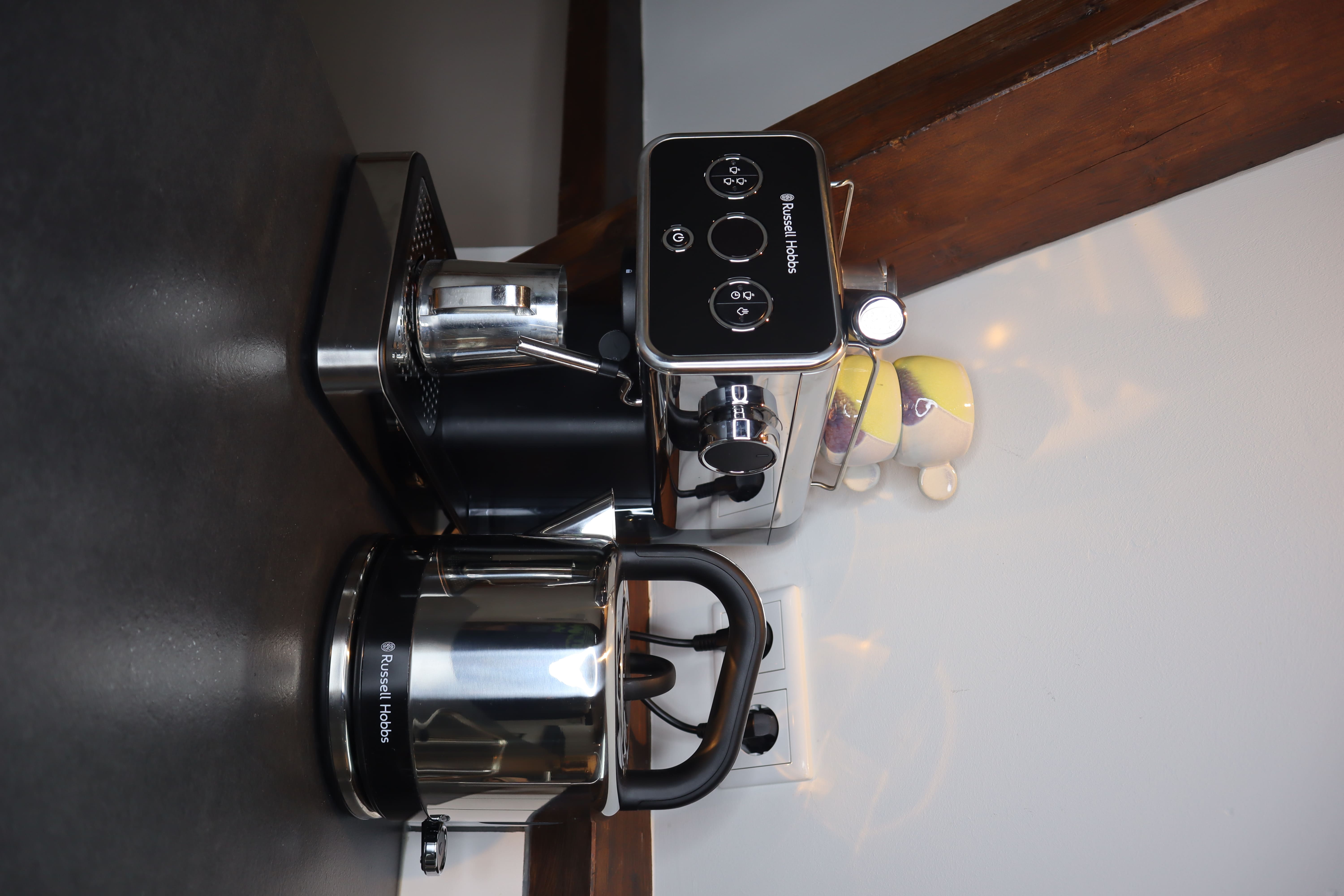 Keuken met zwarte werkbladen, een koffiezetapparaat en een waterkoker naast een muur met tegels.