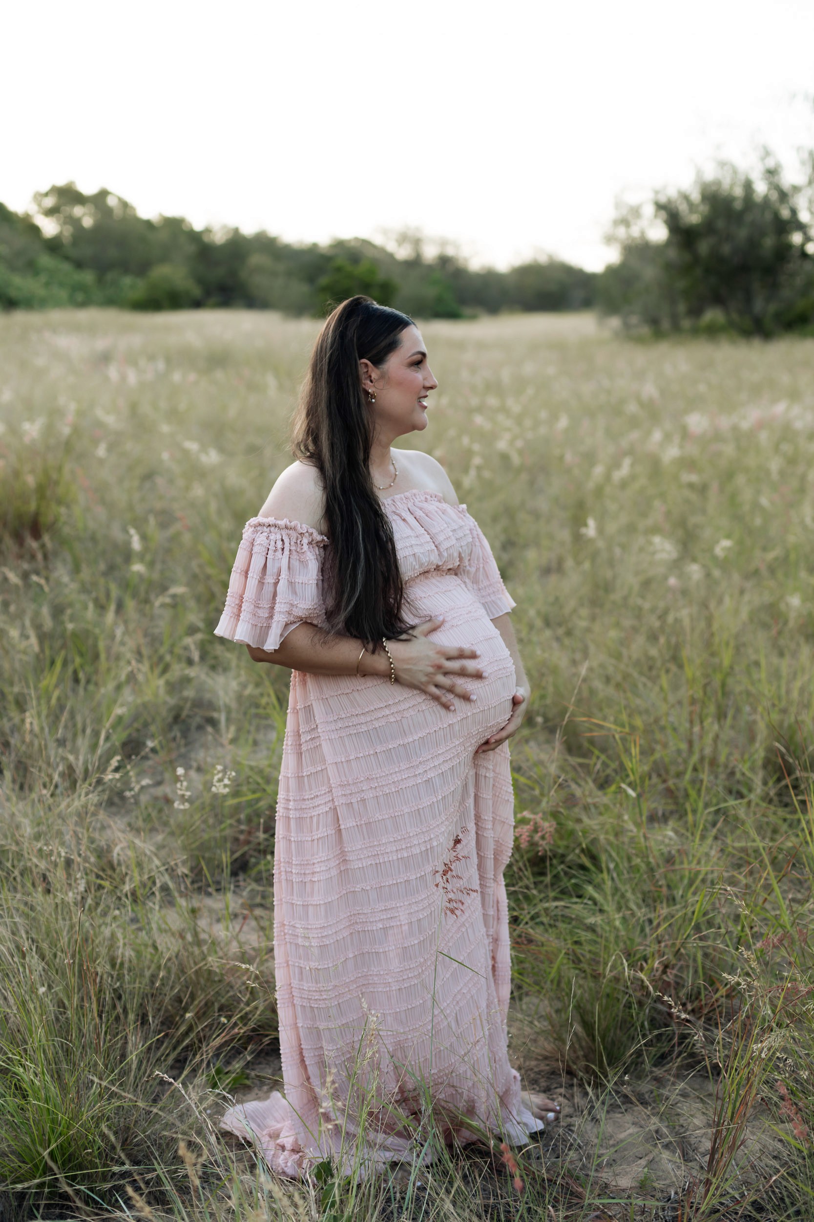 Mackay maternity session featuring pregnant woman in long grass at golden hour wearing elegant flowing dress