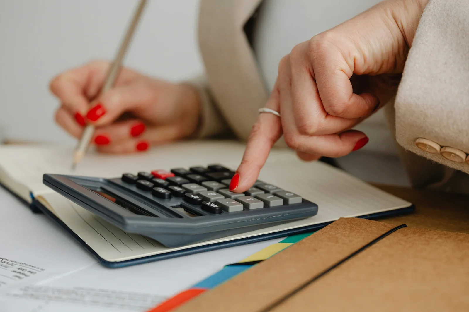 Woman with red nails using calculator at desk with financial documents and notebook for budget planning.