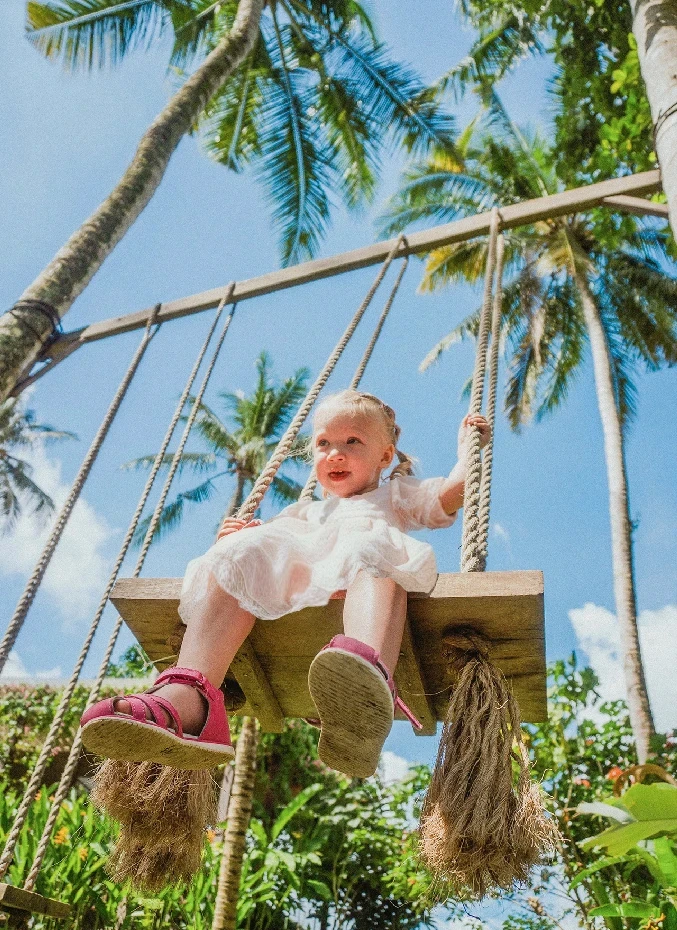 A little girl wearing white dress swinging