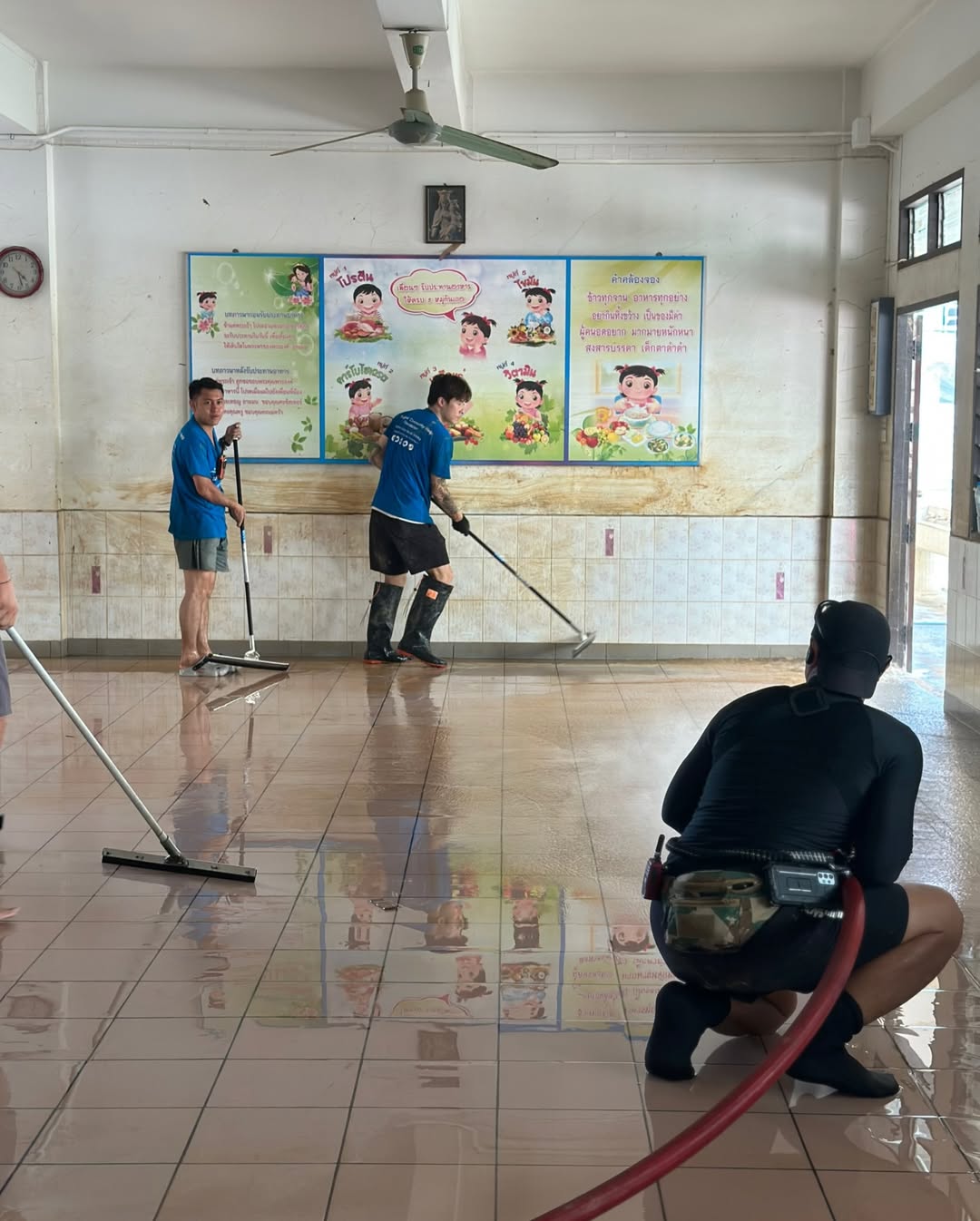 man in blue t-shirt and white floral skirt holding black smartphone while sitting on sidewalk